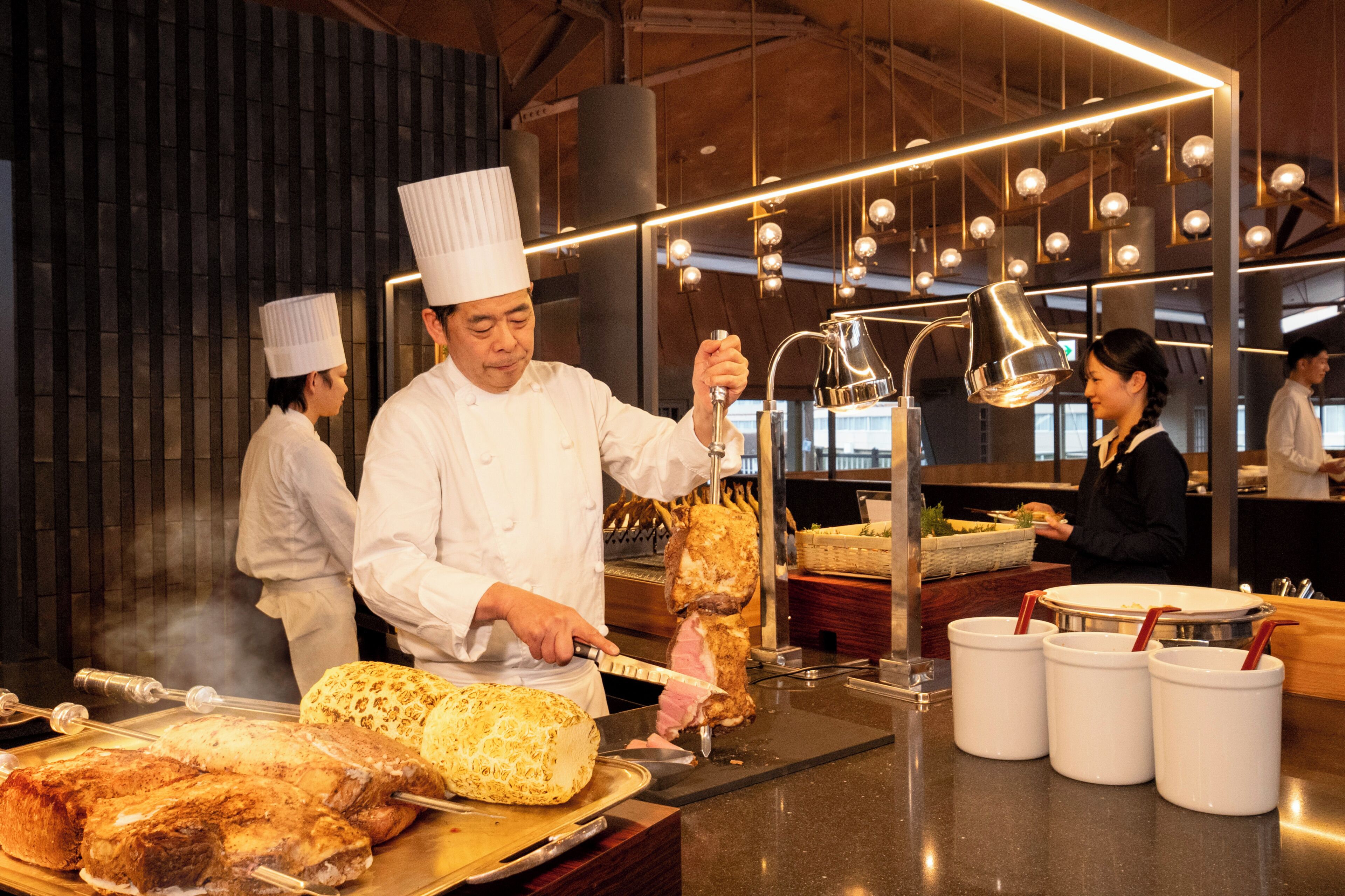 A chef preparing food in a modern kitchen with hanging lights and a counter with food items.