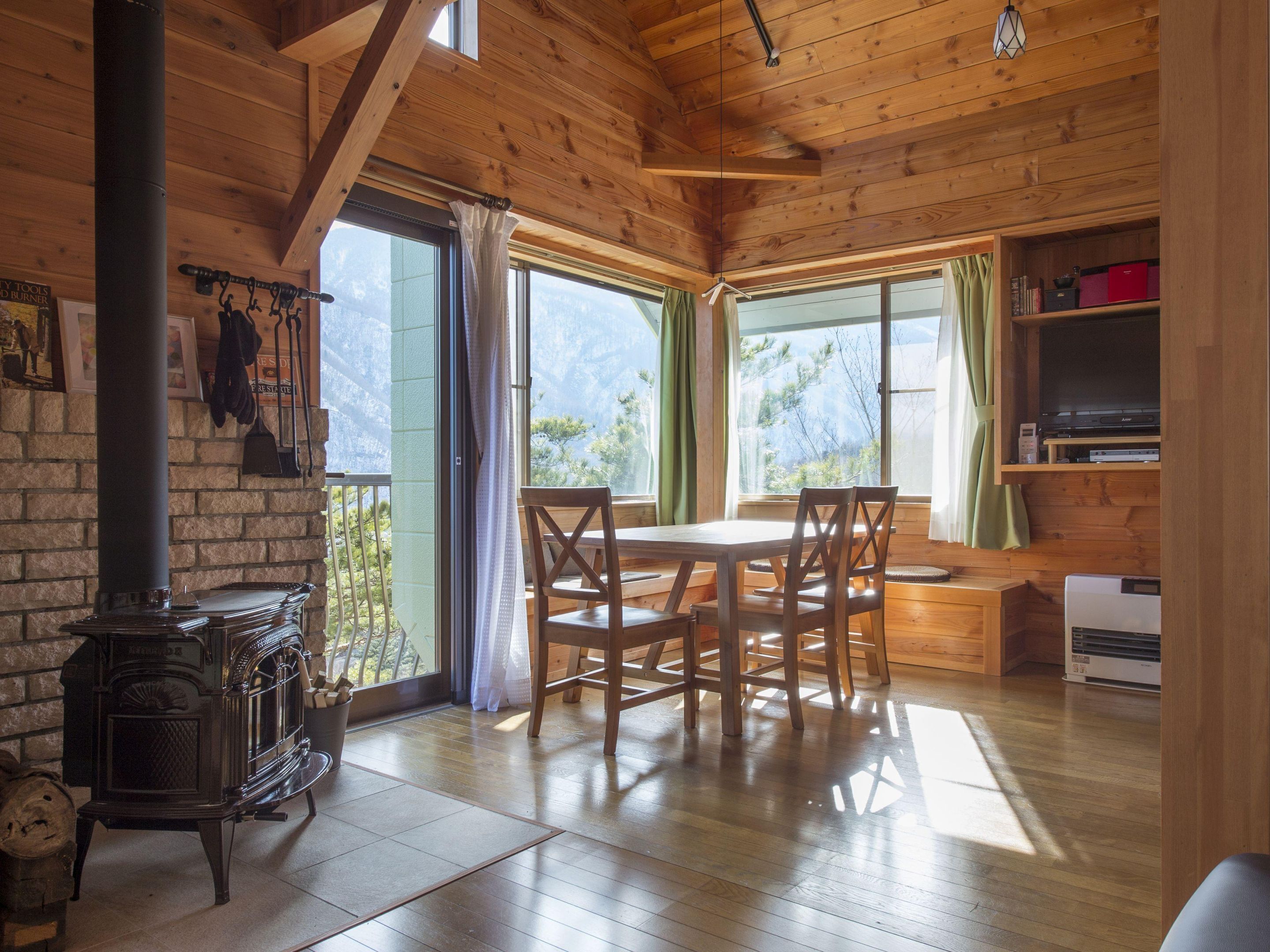 A wooden cabin interior with a dining table, chairs, a fireplace, and a TV shelf.
