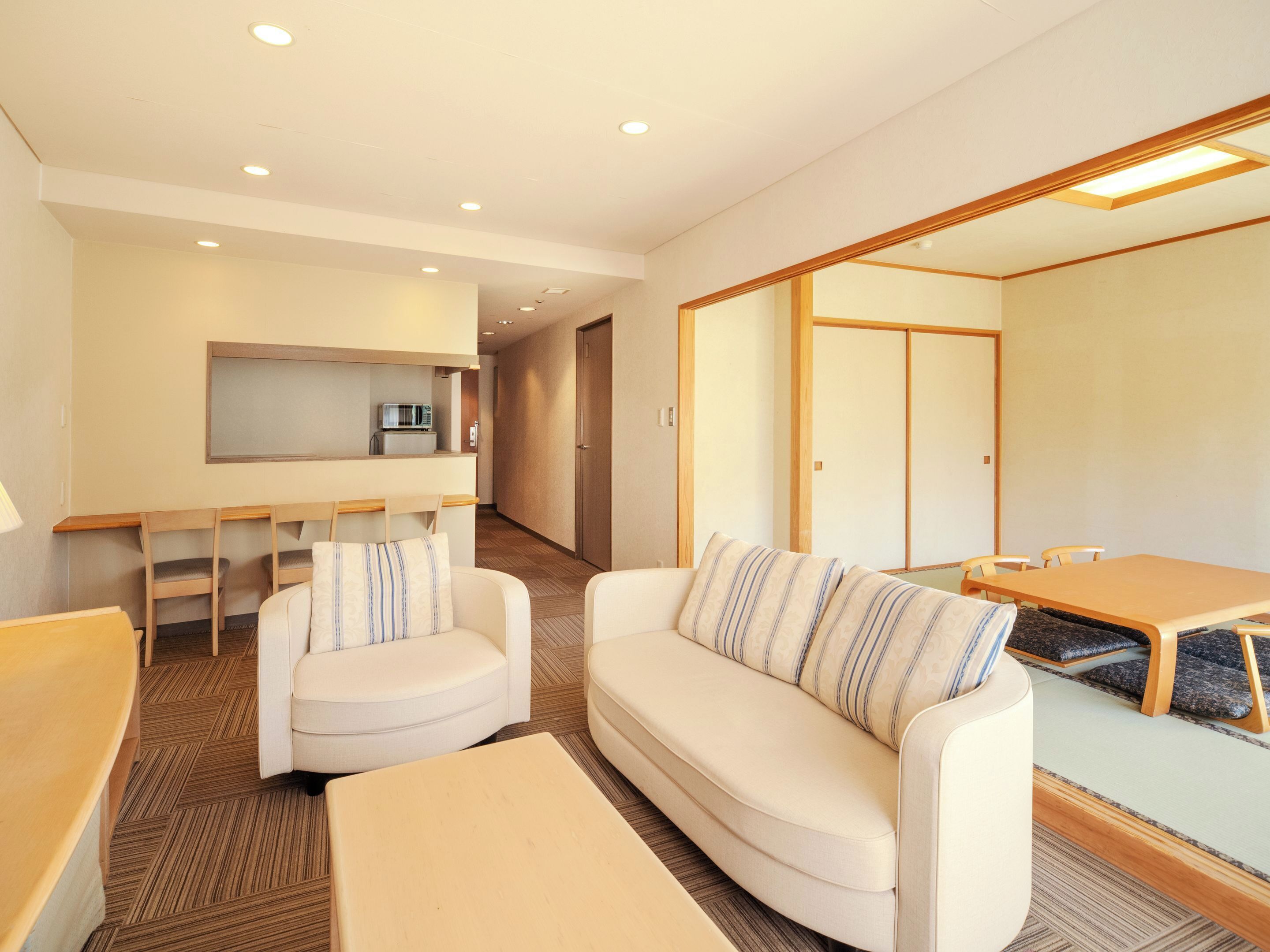 A modern hotel room with a sofa, a small table, a kitchenette, and a sliding door closet.