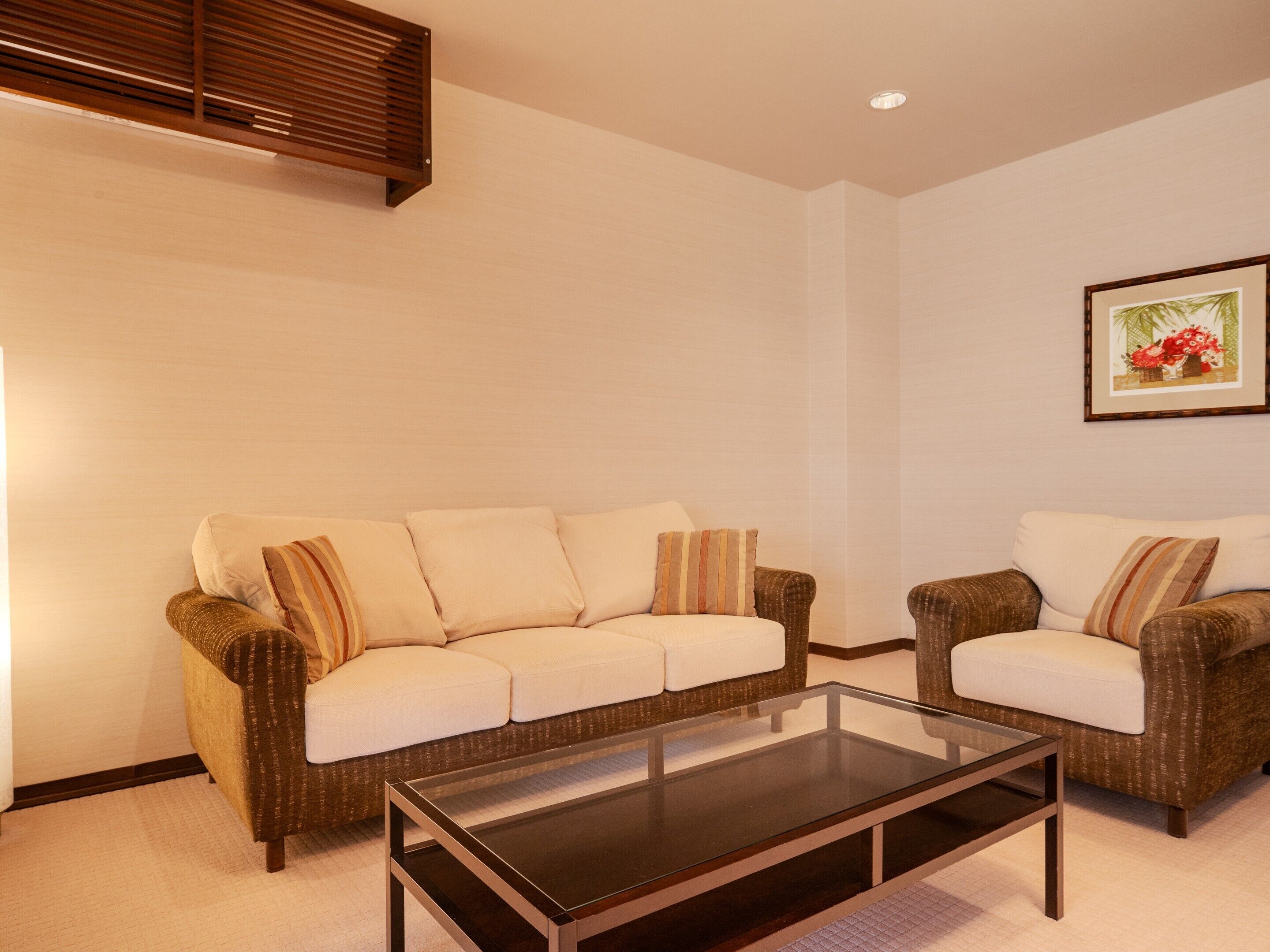 A living room with a sofa, armchair, and a glass coffee table.