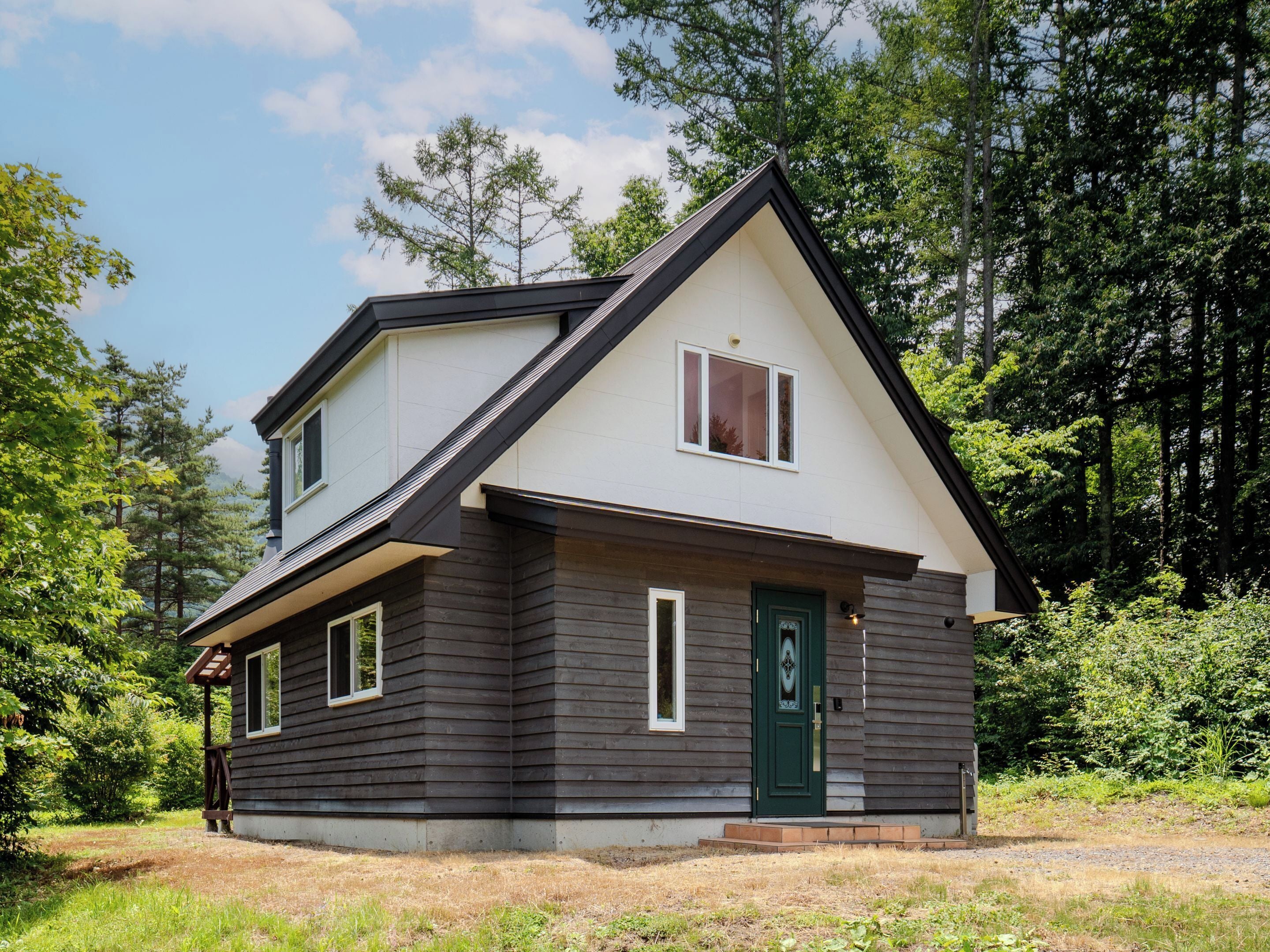 Ein zweistöckiges Haus mit dunkler Fassade, einer grünen Tür und einer kleinen Veranda.