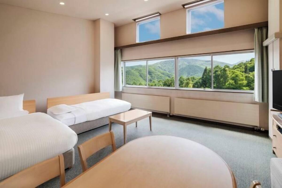 Ett hotellrum med ett stort fönster, en säng, en soffa, ett bord och en tv.