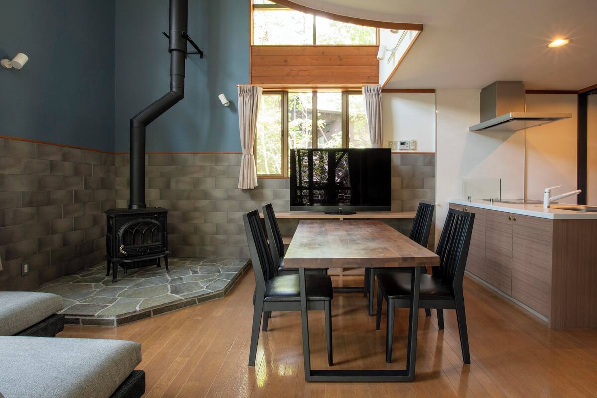 A modern kitchen with a built-in stove, a dining area with a wooden table and chairs, and a large window providing natural light.