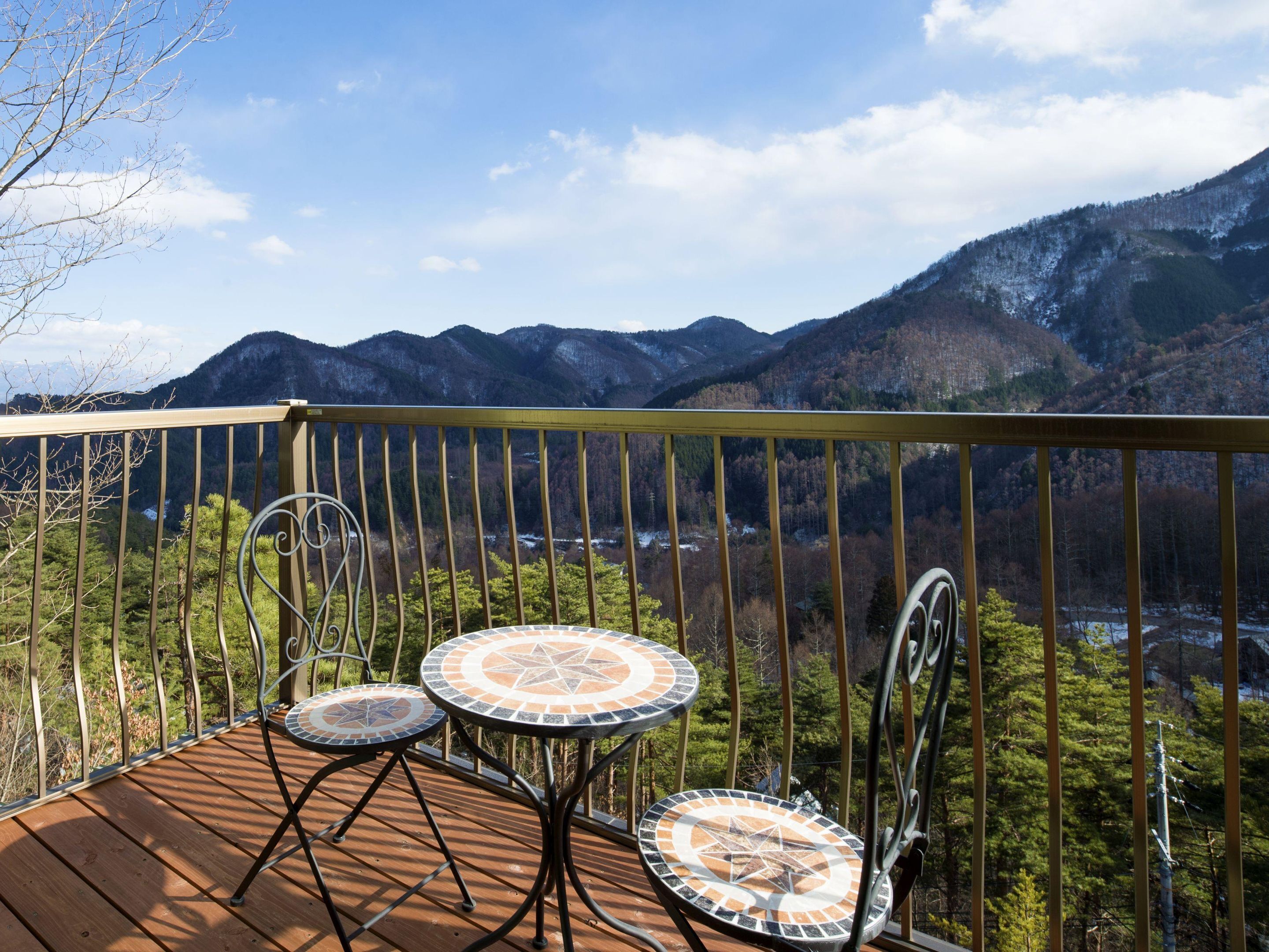 Une terrasse en bois avec deux tables et des chaises ornées de motifs en mosaïque, offrant une vue sur un paysage montagneux.