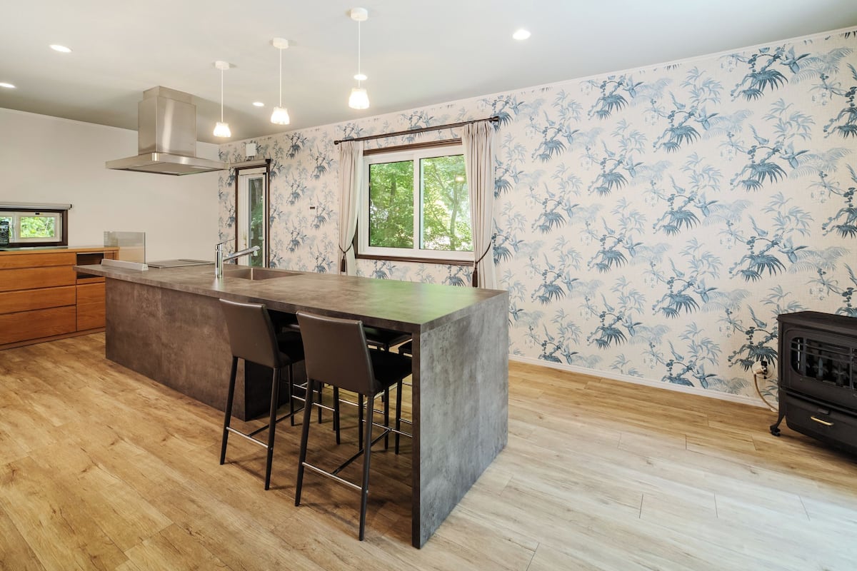 A modern kitchen with a central island, bar stools, a stove, and a window with a view of greenery.