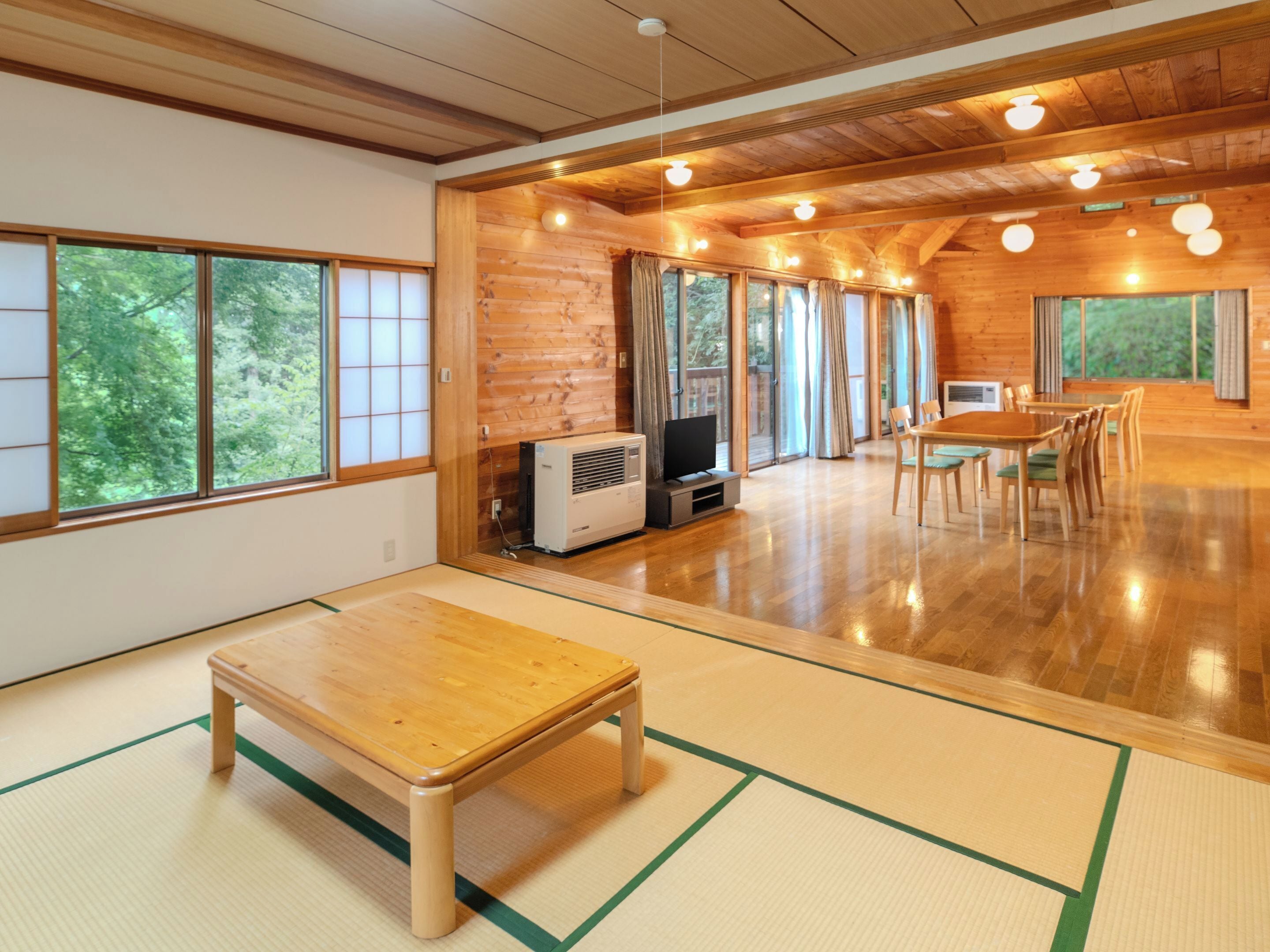 Una habitación amplia con suelo de madera, tatami y una mesa de madera, además de un televisor.
