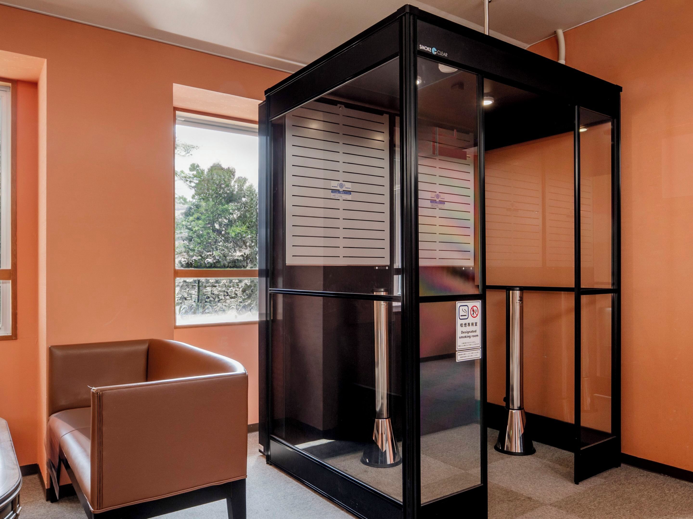 Una habitación moderna con separador de vidrio, un sillón de cuero marrón y ventana con vista a árboles.