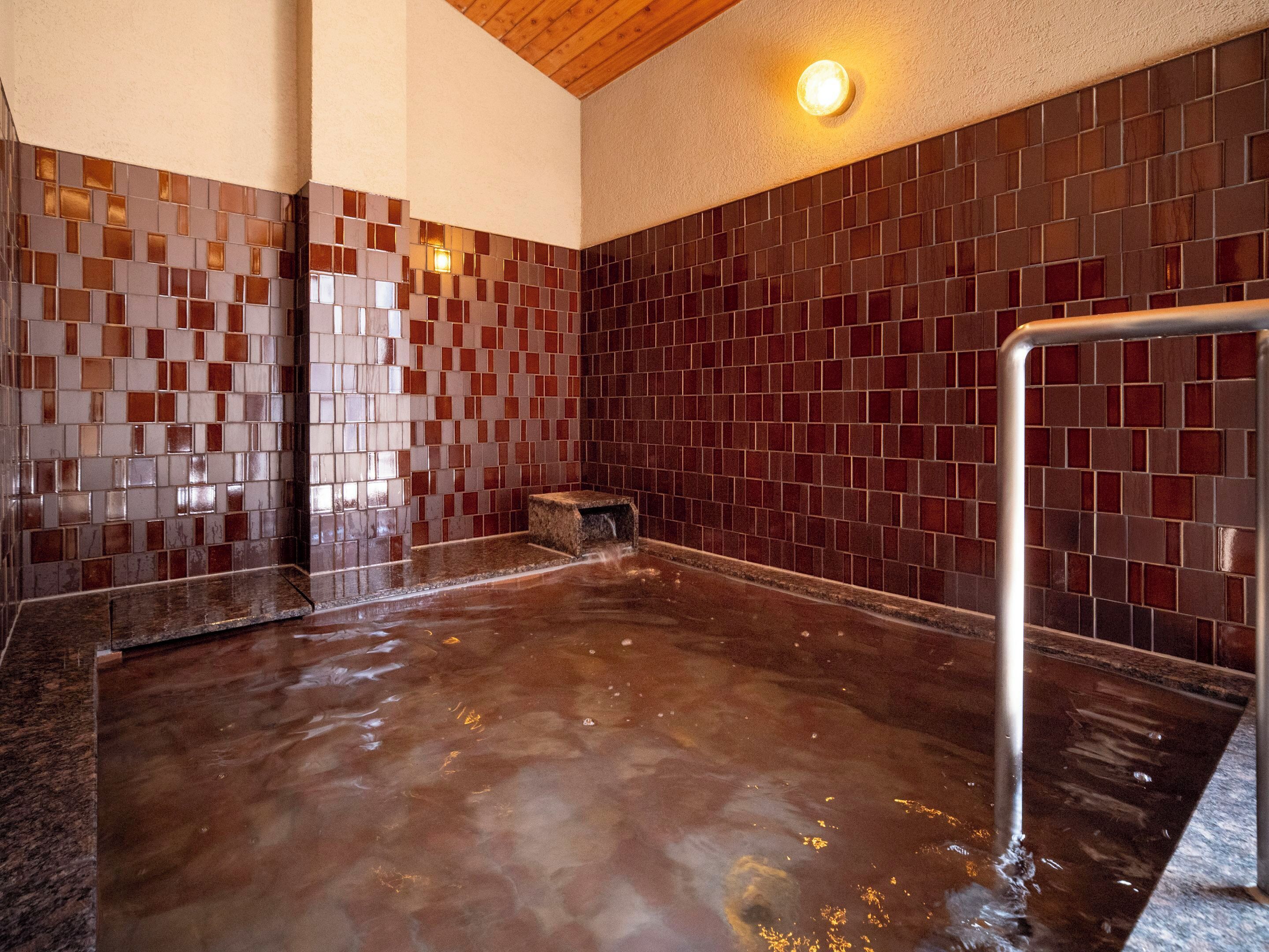 A wet floor in a room with tiled walls and a metal bench.