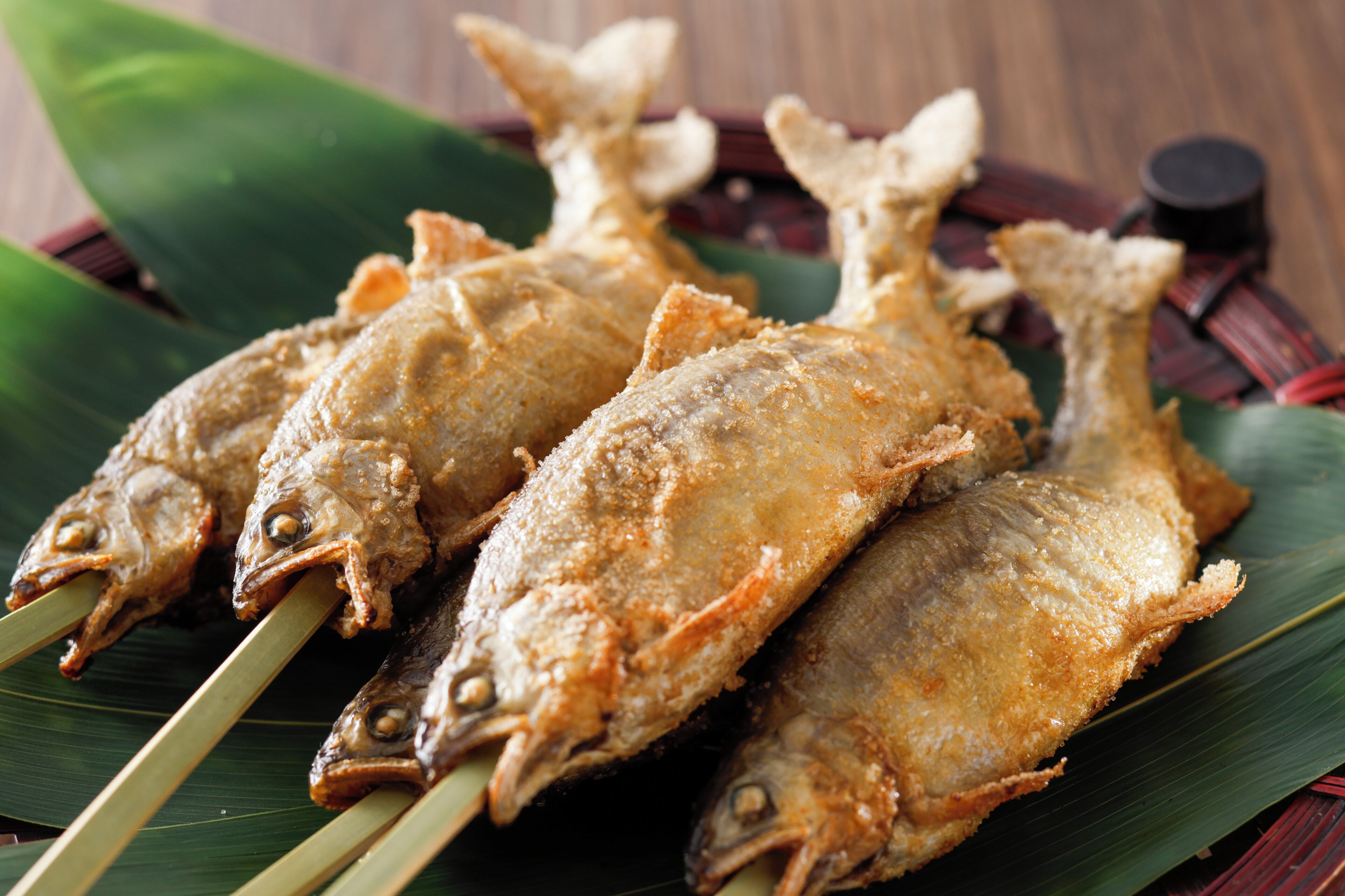 Three fried fish on skewers with a green leaf underneath.