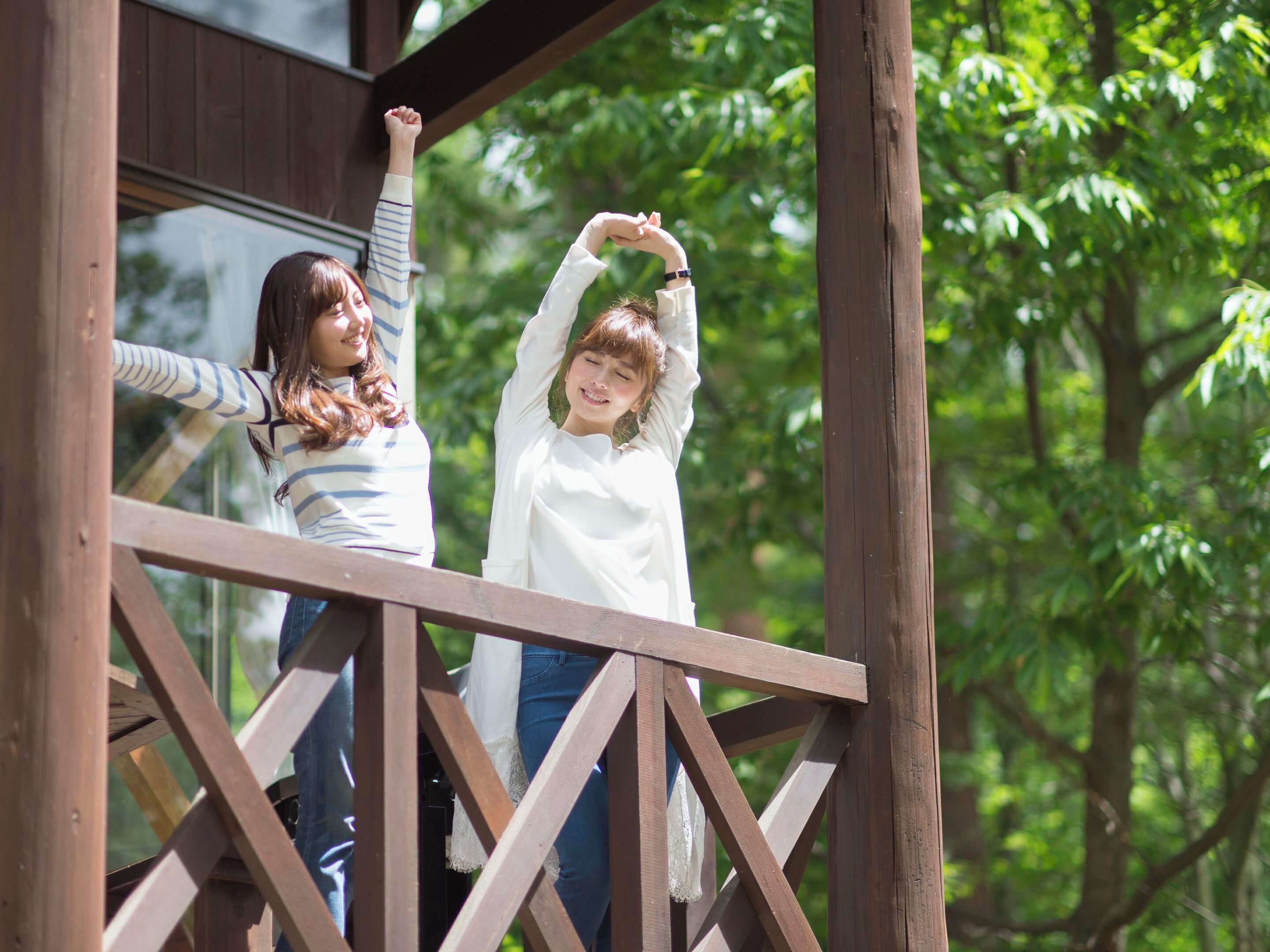 Two individuals on a wooden deck with a lattice railing, surrounded by greenery.