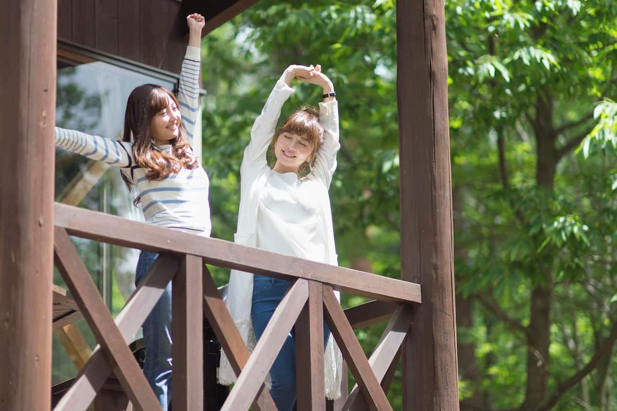 Two individuals on a wooden deck with a lattice railing, surrounded by greenery.
