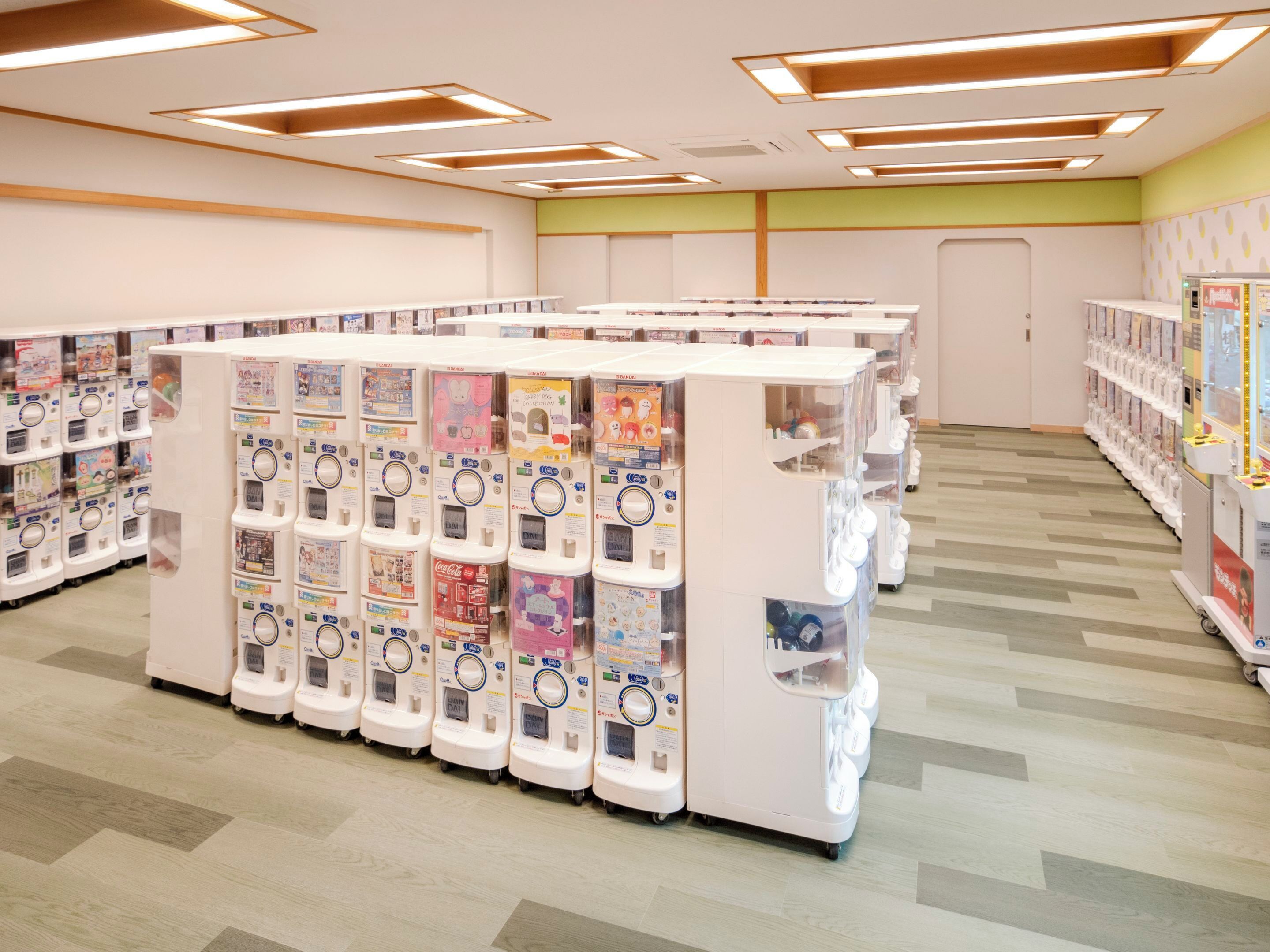 A row of vending machines with various items, a wooden floor, and a green wall.