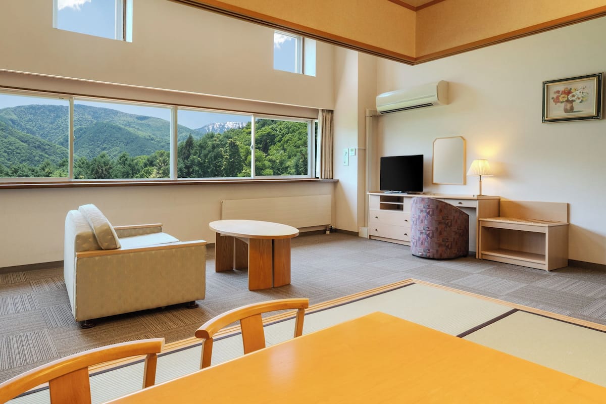 A hotel room with a sofa, a small table, a TV, a lamp, and a view of mountains.