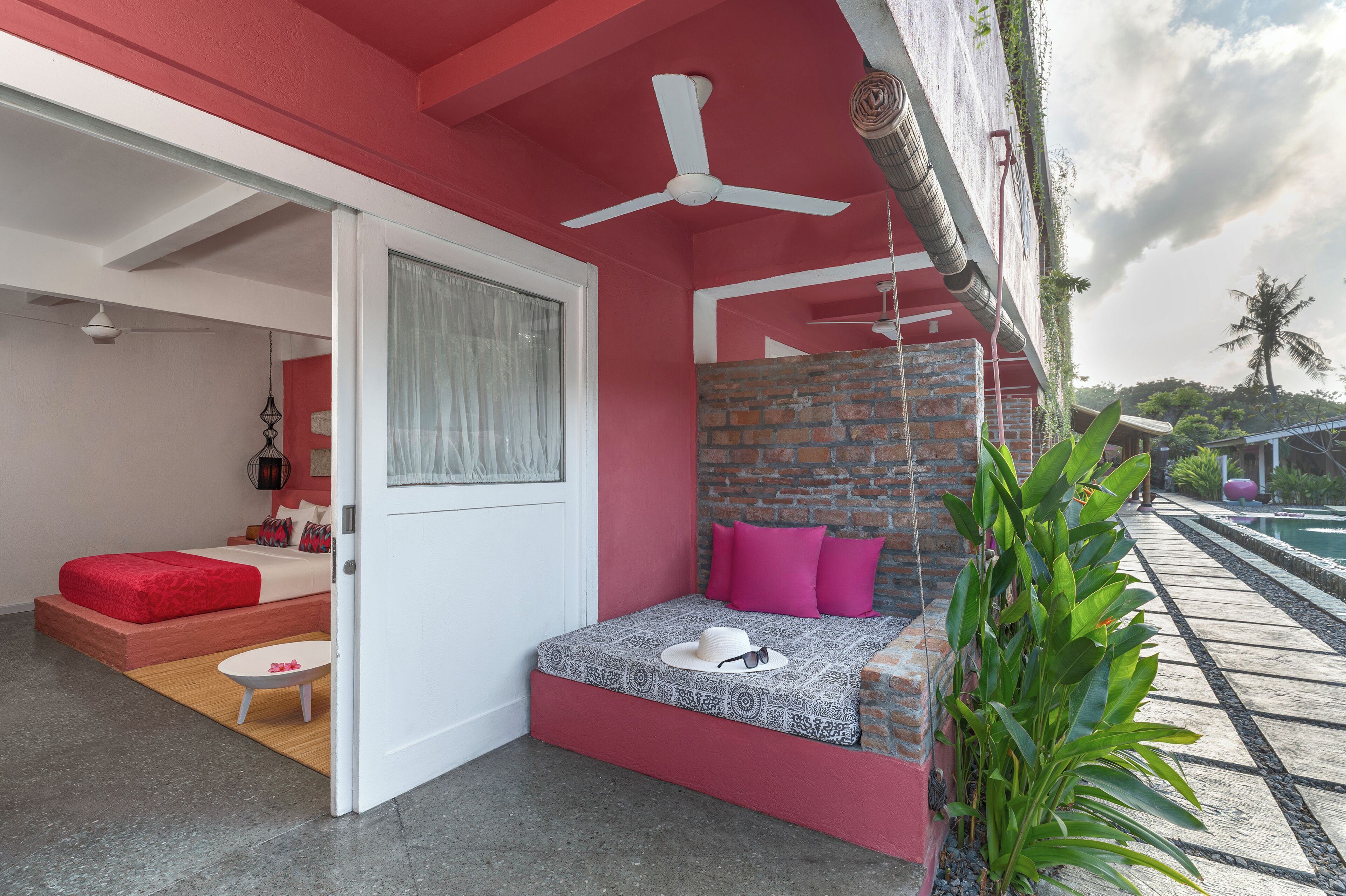 A bedroom with a red and white color scheme, a brick accent wall, a ceiling fan, and a view of a pool.
