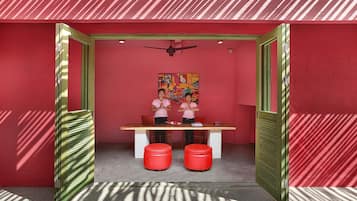 A room with a red wall, a ceiling fan, a table with two red ottomans, and a colorful painting on the wall.