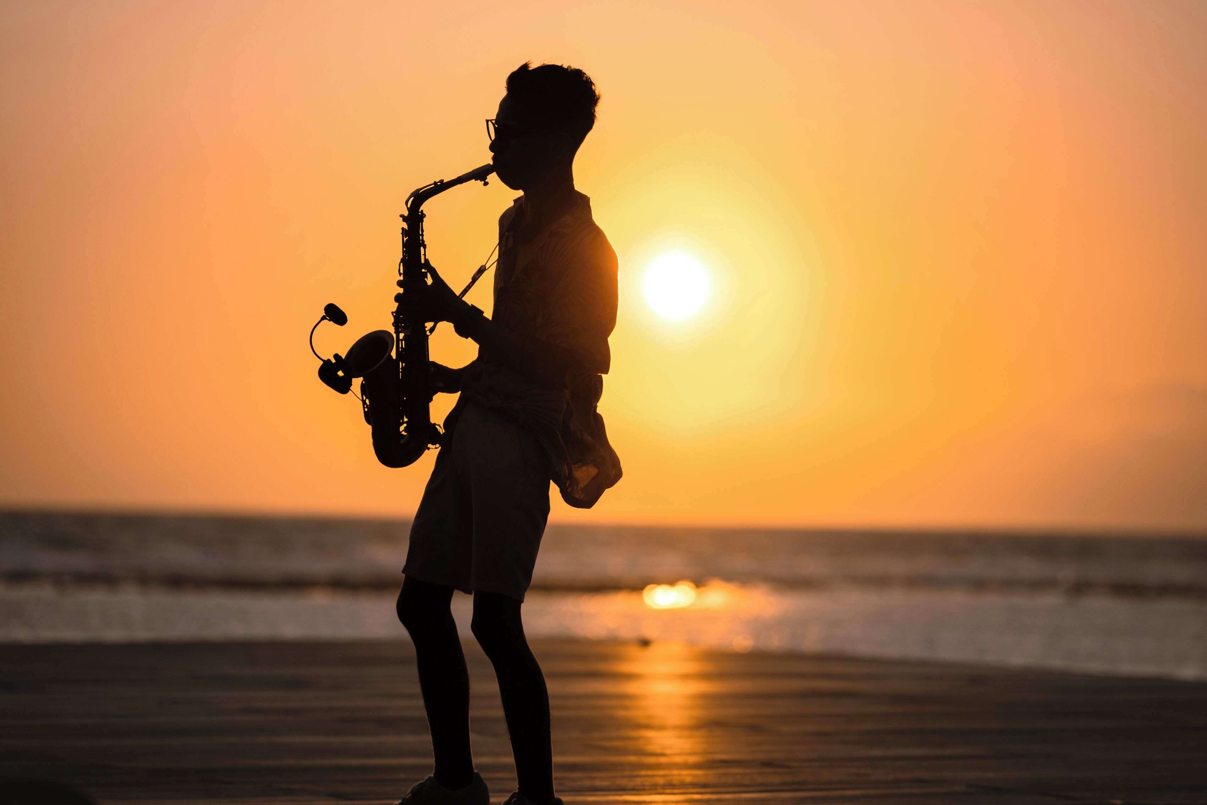 A person playing a saxophone on a beach at sunset.