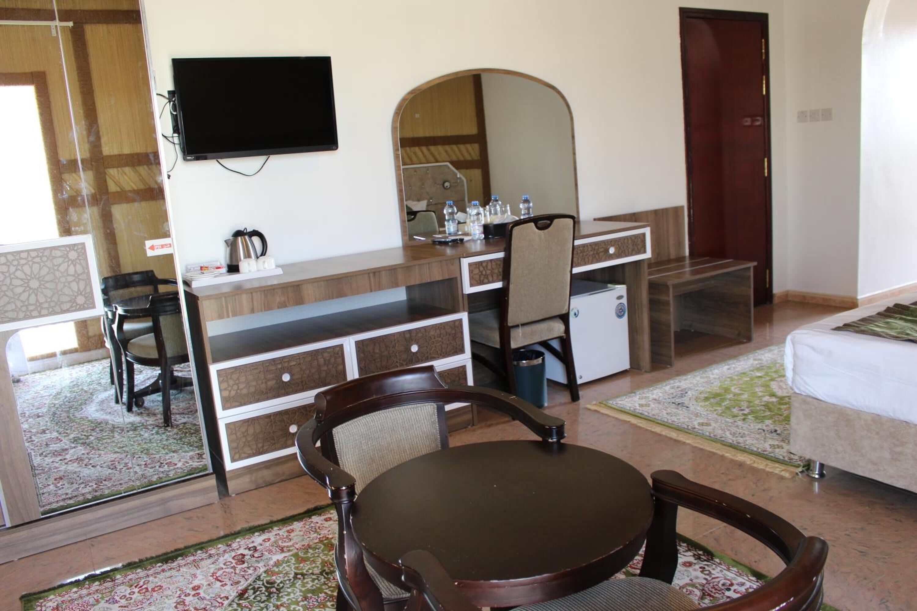 Habitación de hotel con cama, escritorio con silla, televisión, espejo y una pequeña mesa con una silla.