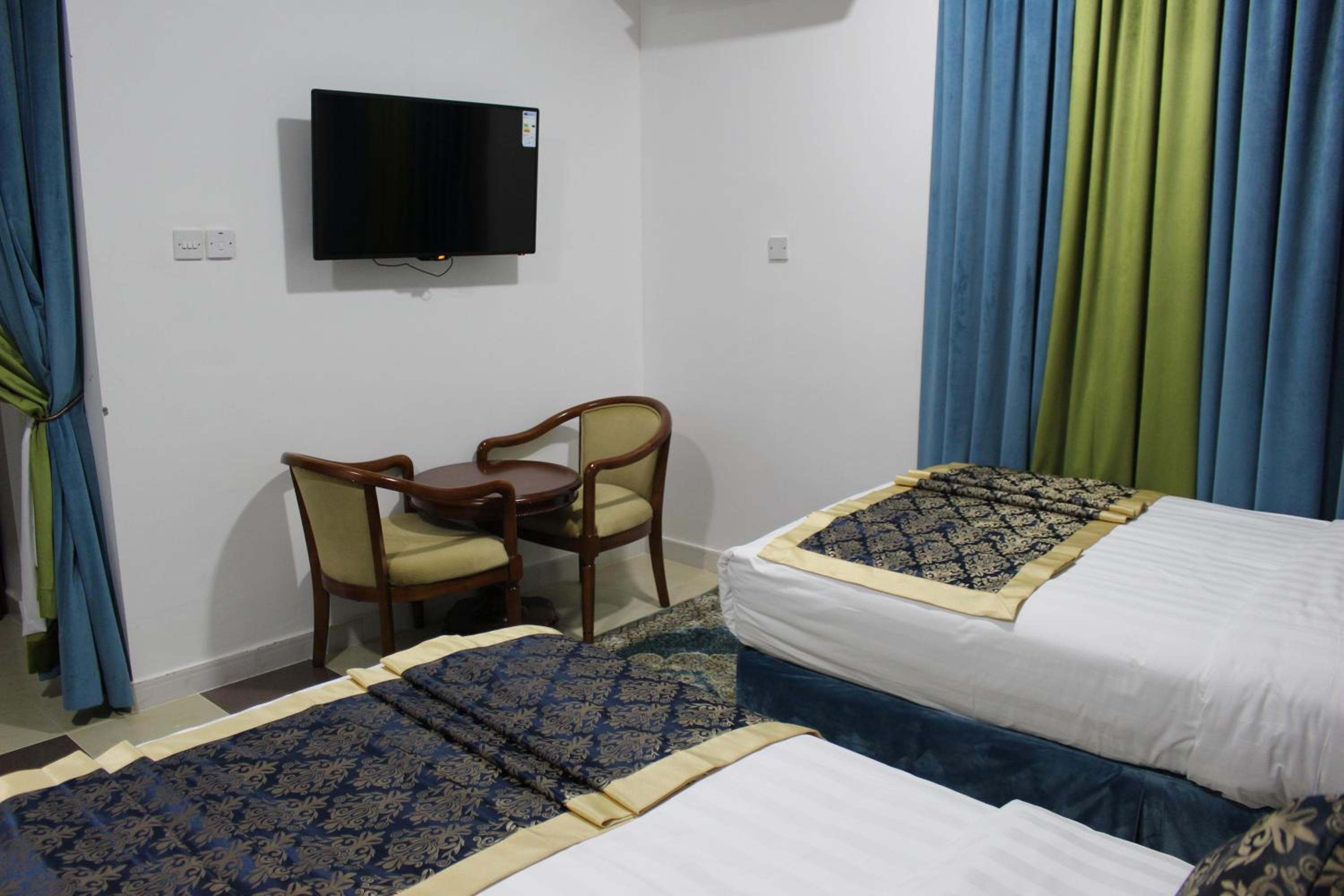 Een hotelkamer met twee bedden, een bureau, een stoel, een televisie en gordijnen.