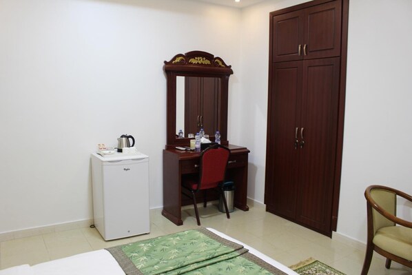 A compact hotel room with a single bed, a small desk with a chair, a wardrobe, and a mini-fridge. - Aldiyar Hotel (Nizwa)