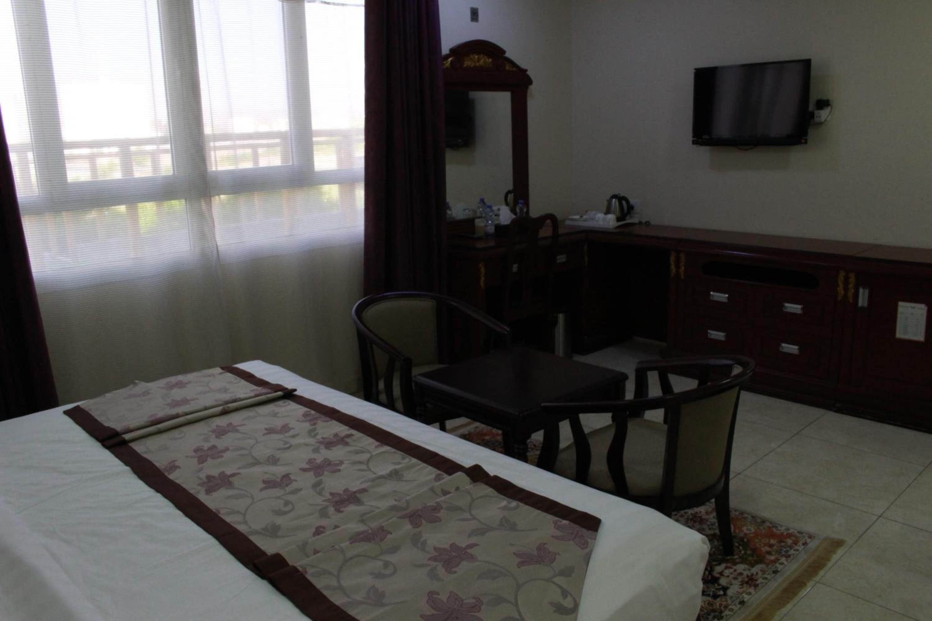 A hotel room with a bed, a desk, a chair, a television, and a window with curtains.