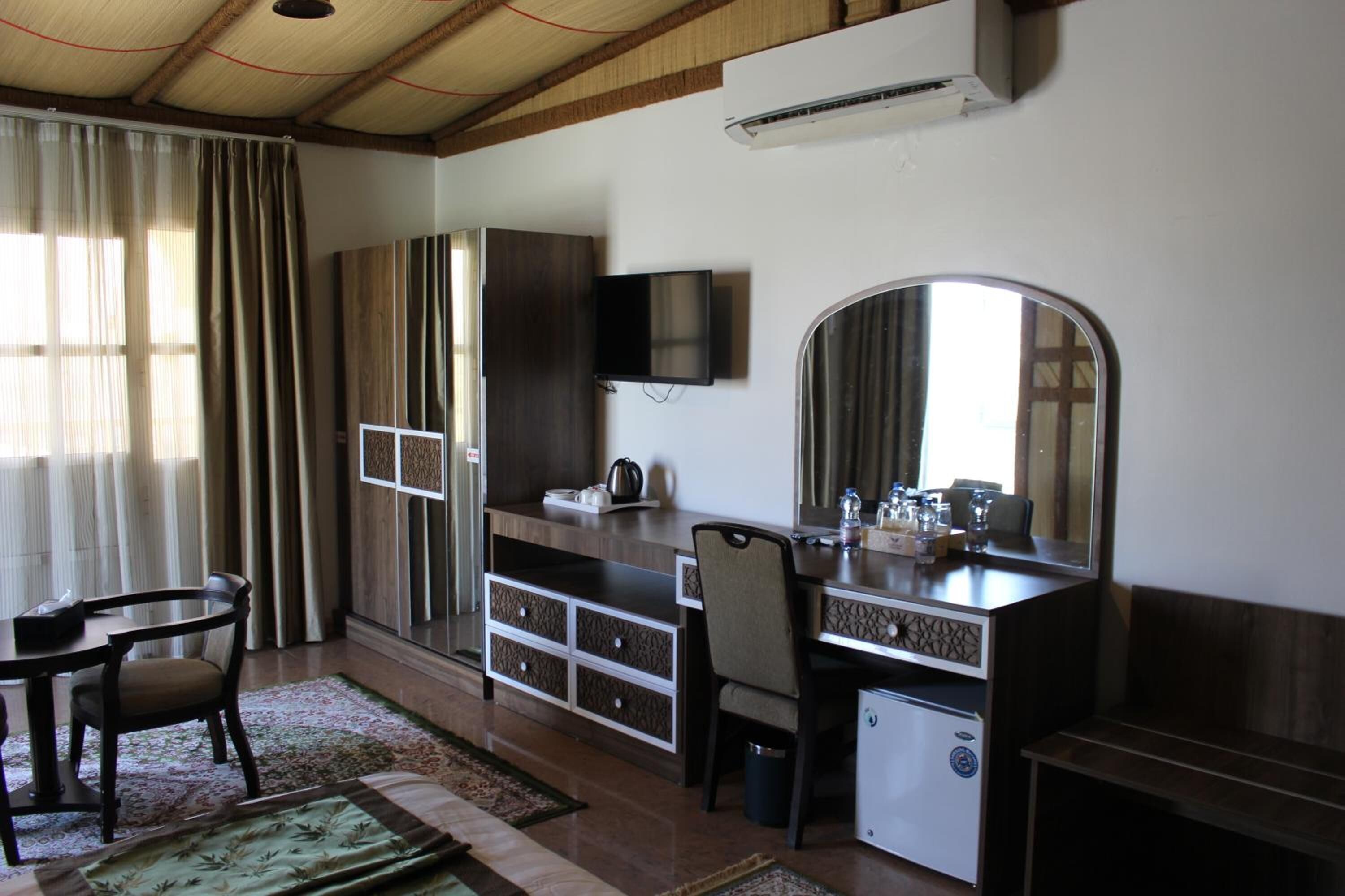 Une chambre d’hôtel équipée d’un bureau, d’une chaise, d’une armoire, d’une télévision et d’un petit réfrigérateur.