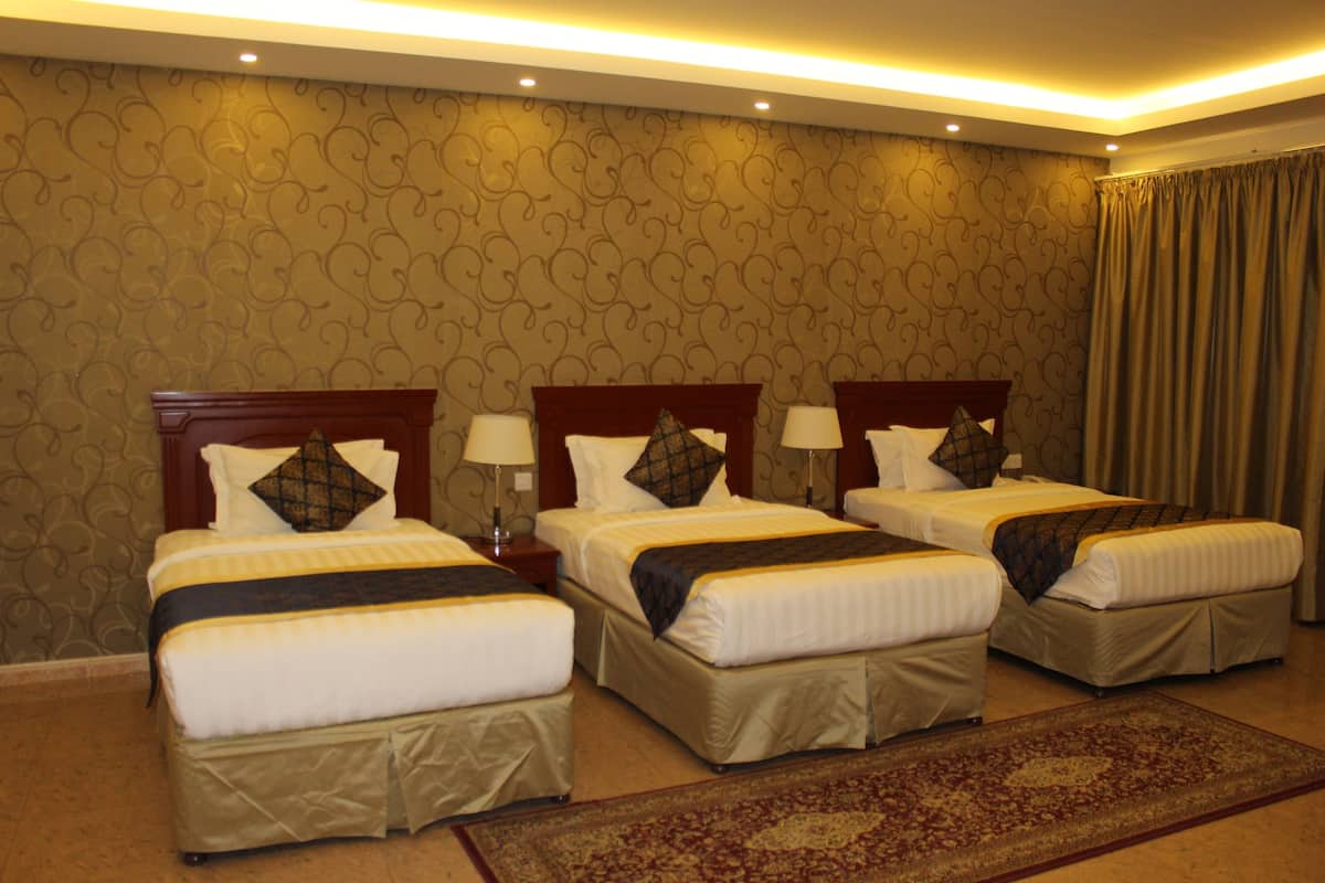 A hotel room with three beds, each with a wooden headboard, white bedding, and a patterned carpet.