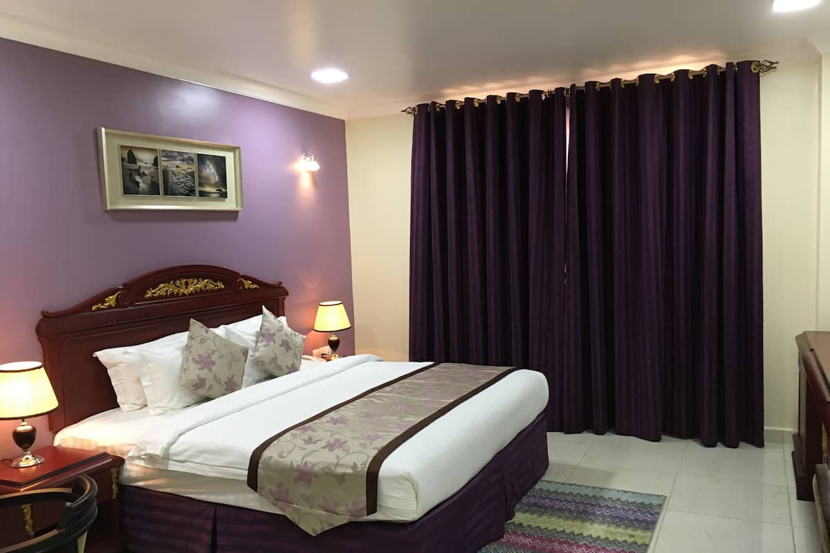 A neatly made bed with a headboard, two bedside lamps, a nightstand, and a framed picture on the wall.