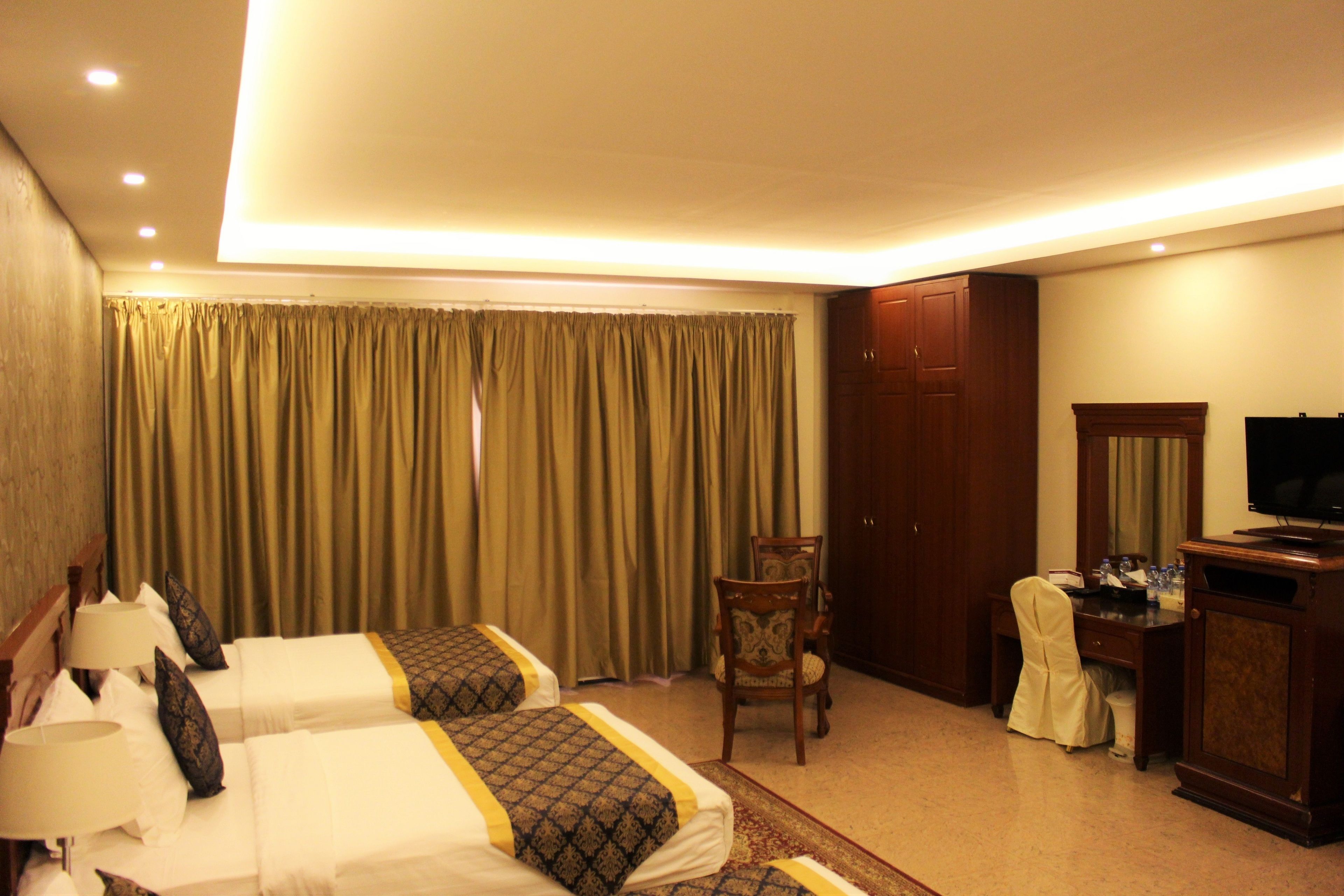 A hotel room with two beds, a desk, a chair, a television, and a wardrobe.