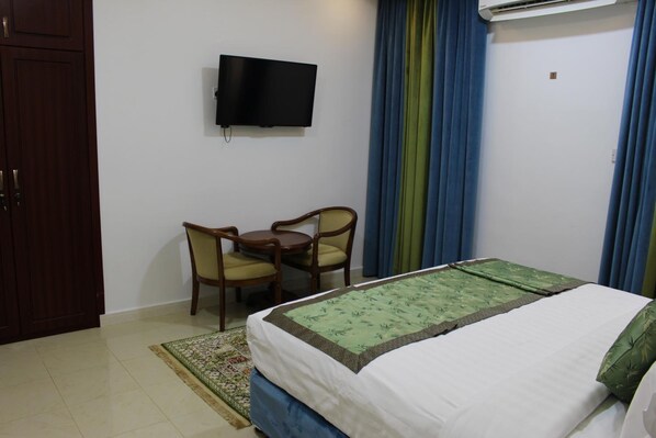 A hotel room with a bed, a TV mounted on the wall, a desk with chairs, and a window with curtains.