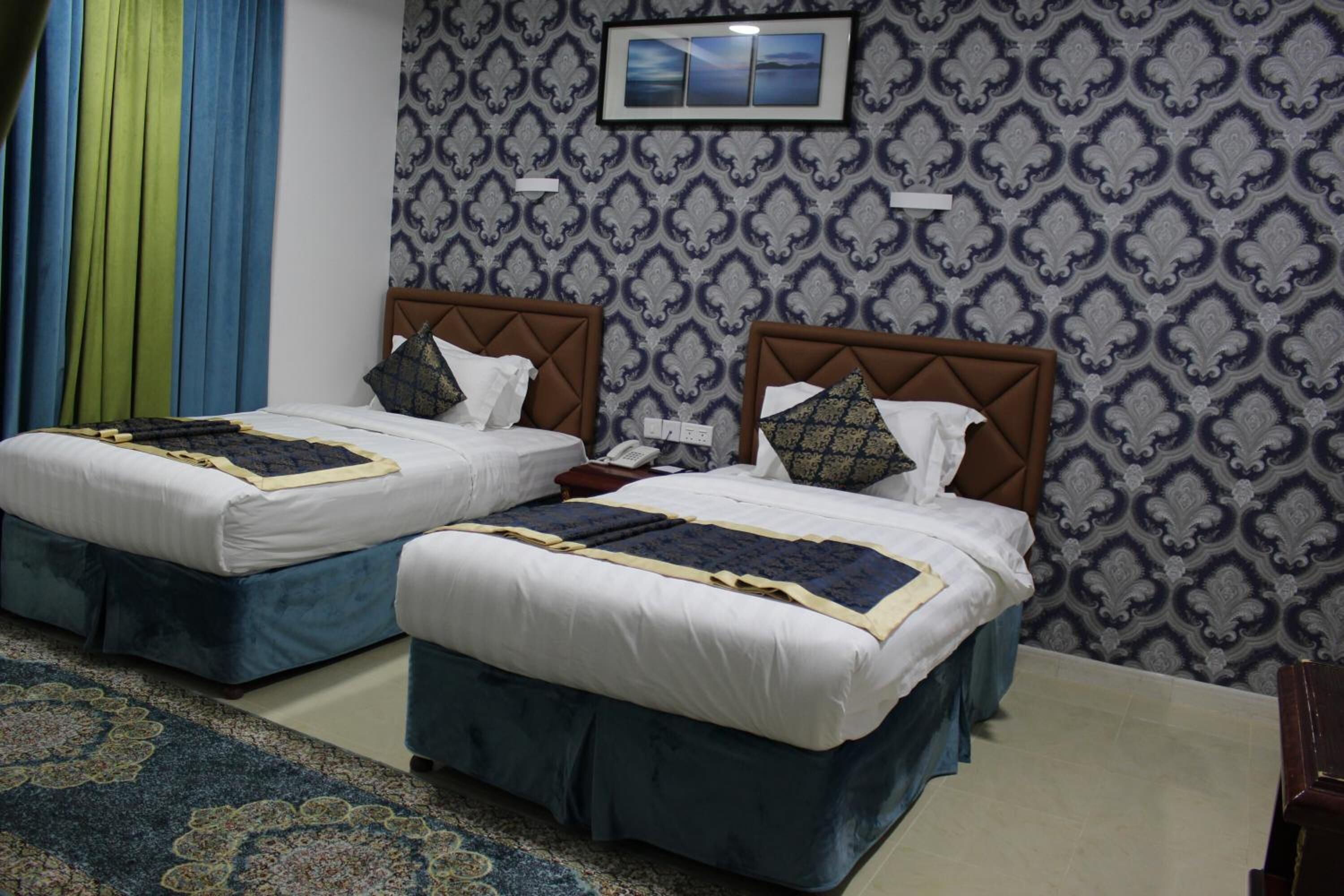 A hotel room with two beds, each with a headboard, a bedside table, and a telephone.