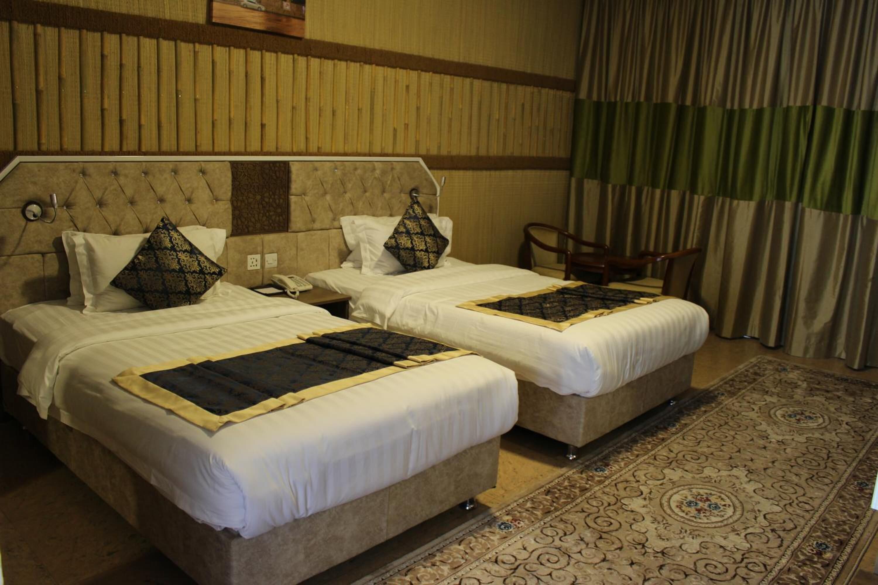 Habitación de hotel con dos camas, un teléfono en la mesita de noche, una silla y una alfombra estampada.