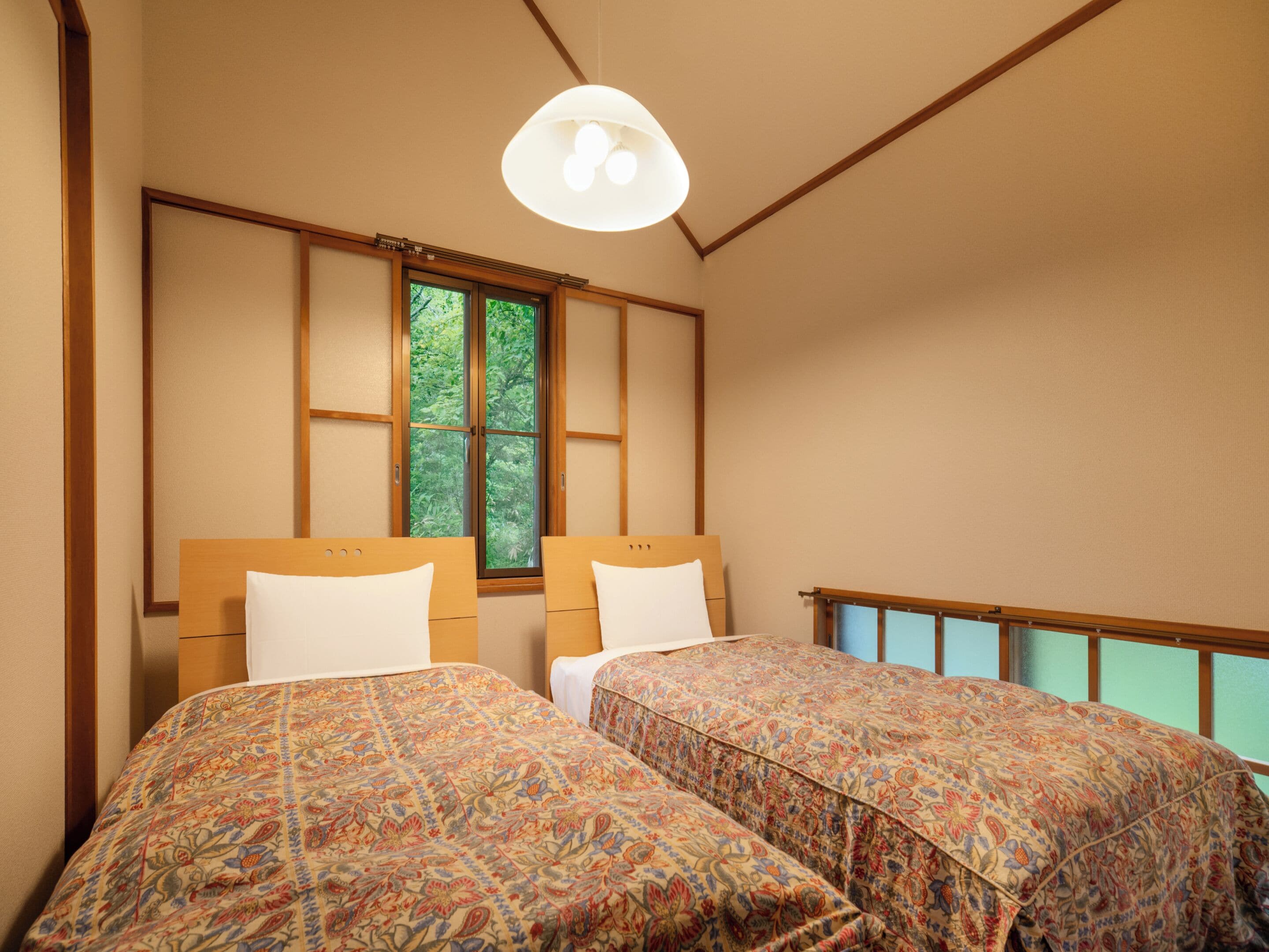 Un dormitorio con dos camas, una ventana con vista a la vegetación y una lámpara colgante.