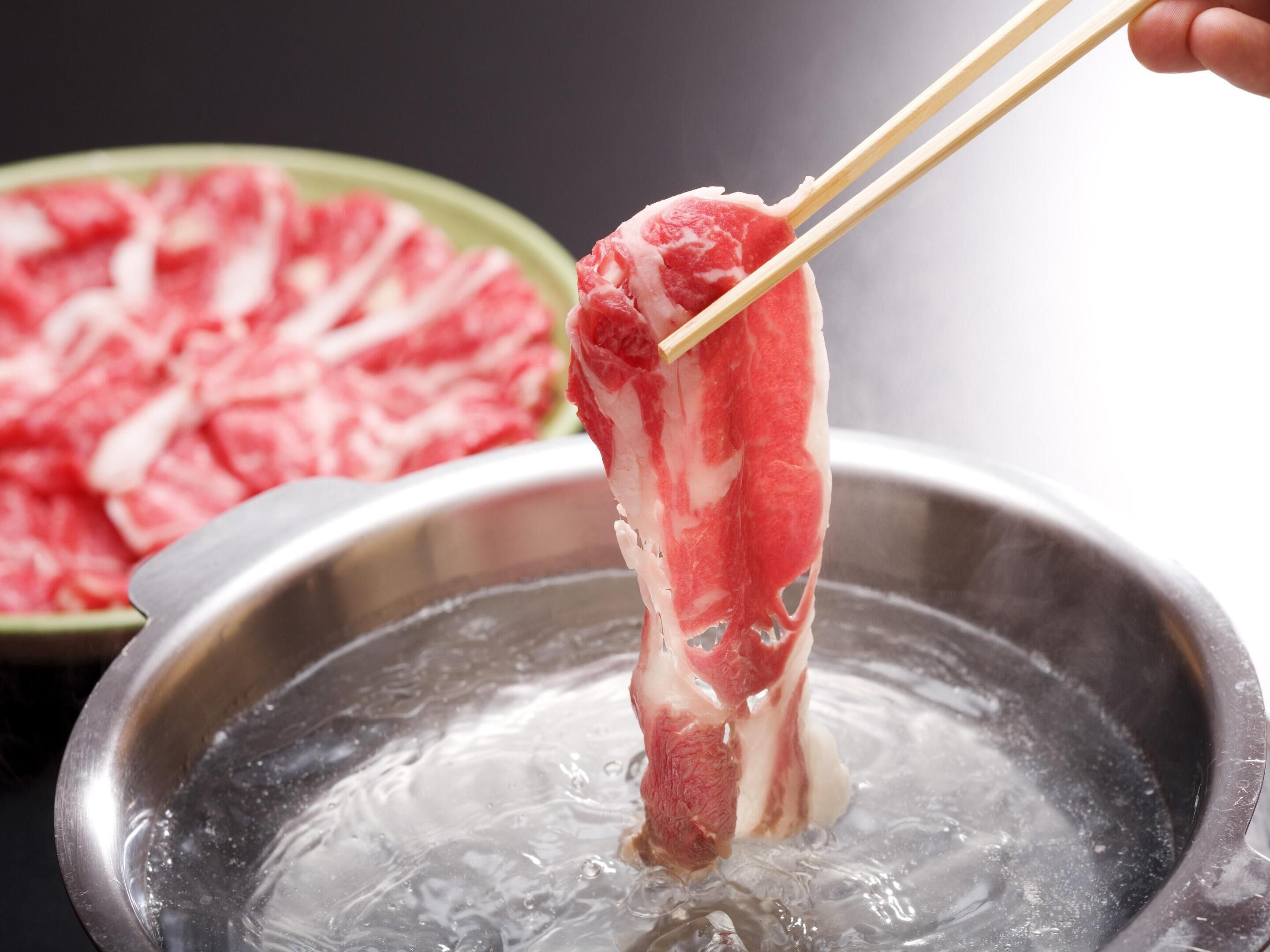 A piece of meat being held by chopsticks over a pot of boiling water.