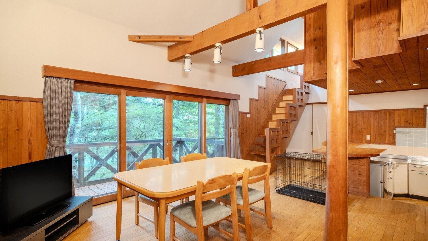 Un intérieur en bois comprenant une table à manger, des chaises, un téléviseur, un escalier et un coin cuisine.