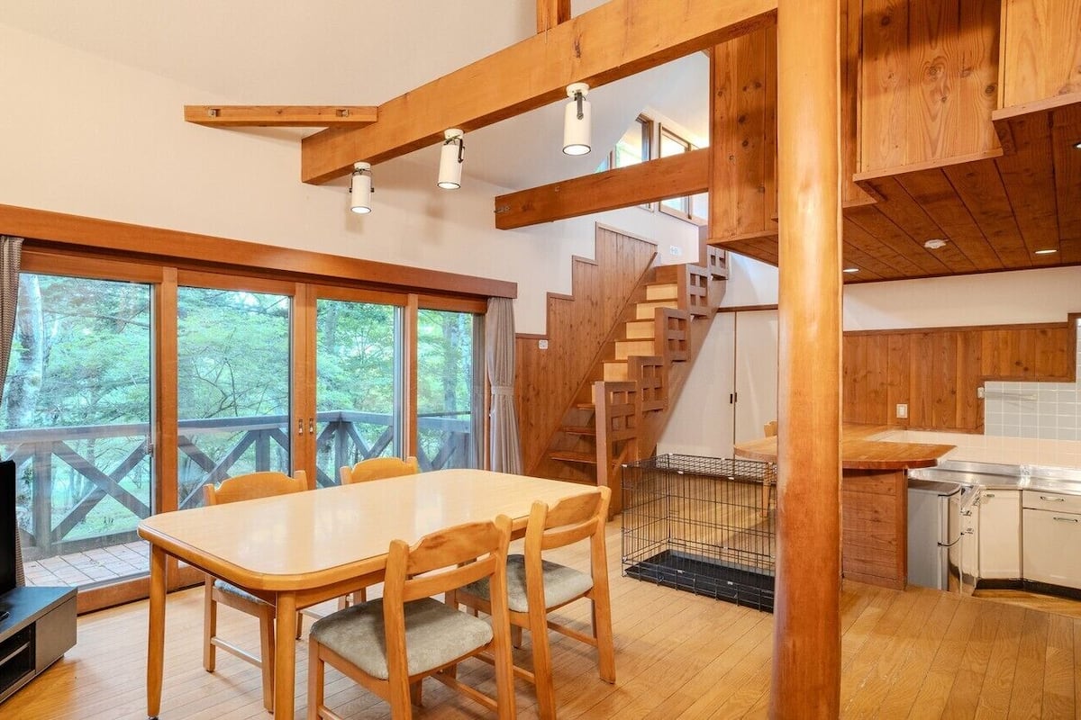 A wooden interior with a dining table, chairs, a TV, a staircase, and a kitchen area.