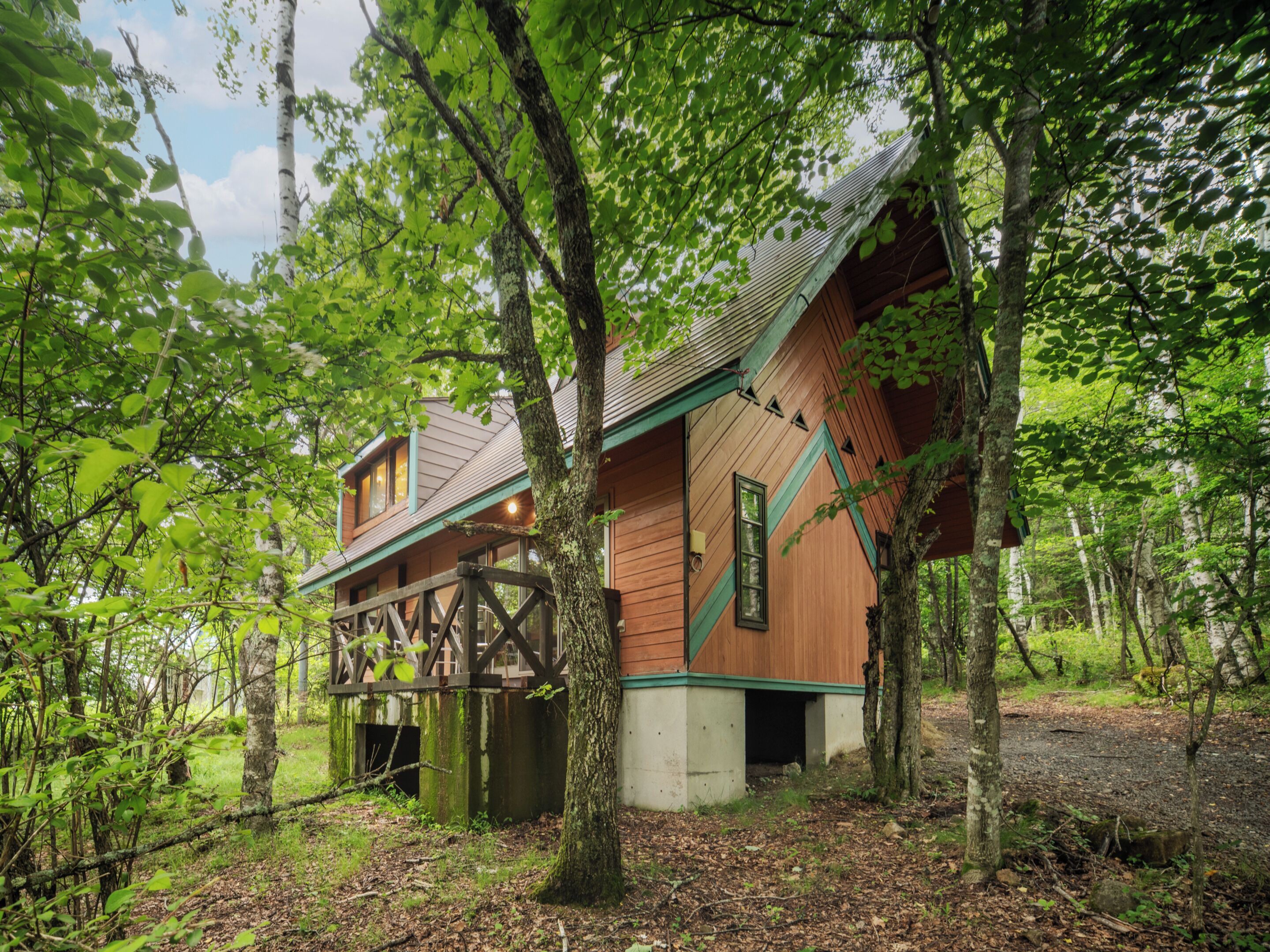 A wooden cabin with a deck, surrounded by trees and forest.