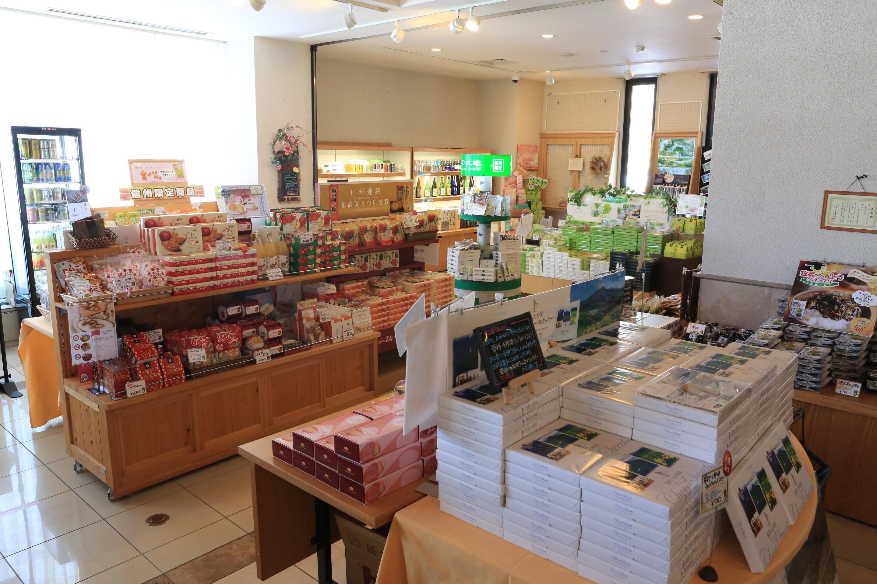 A store interior with shelves stocked with various packaged goods, a display counter with promotional materials, and a refrigerated section in the background.