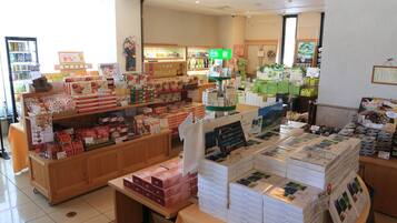 A store interior with shelves stocked with various packaged goods, a display counter with promotional materials, and a refrigerated section in the background.