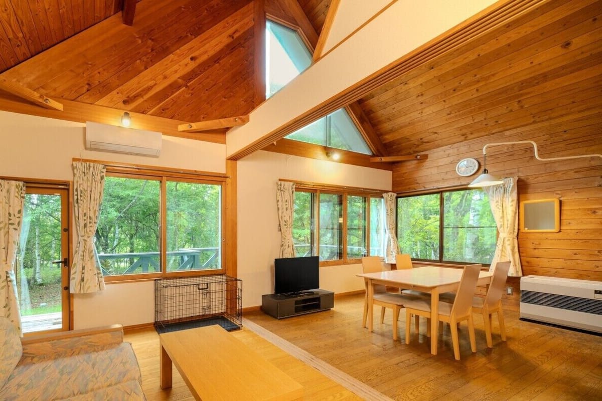 A wooden interior with a dining table, chairs, a TV, and large windows.