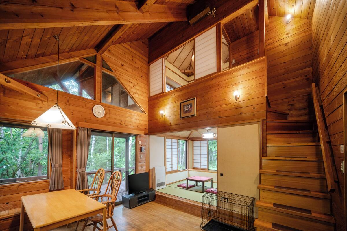 Una cabaña de madera con comedor, televisión y escalera.