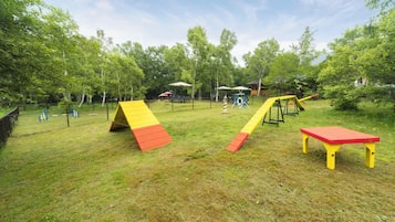 Kids can play on the climbing wall, slide, and swing set in this secure outdoor play area surrounded by trees.