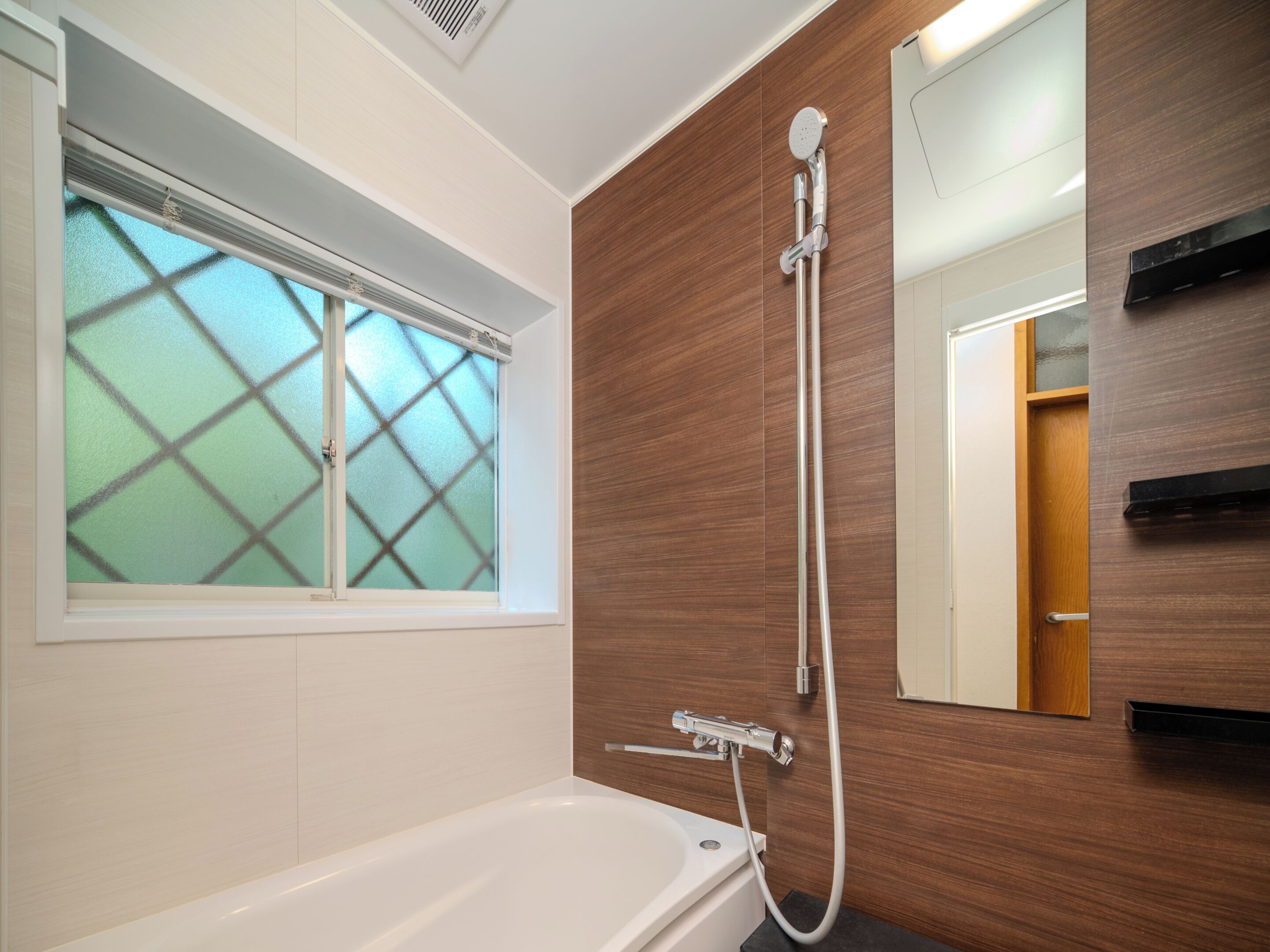 A modern bathroom with a bathtub, a shower, and a window with frosted glass.
