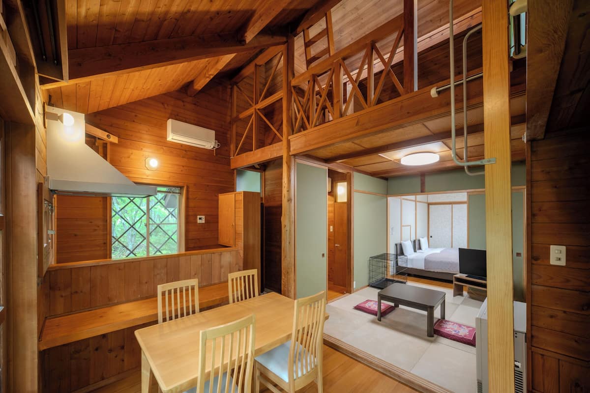Interior de una cabaña de madera con comedor, habitación en altillo y un pequeño salón.