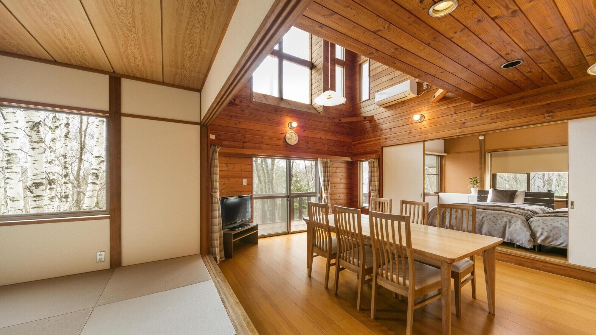 L'intérieur d'un chalet en bois comprend un coin repas, un téléviseur et de grandes fenêtres.