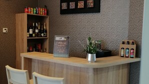 Una mesa de recepción con un reloj, una estantería con bebidas embotelladas y una obra de arte enmarcada encima.