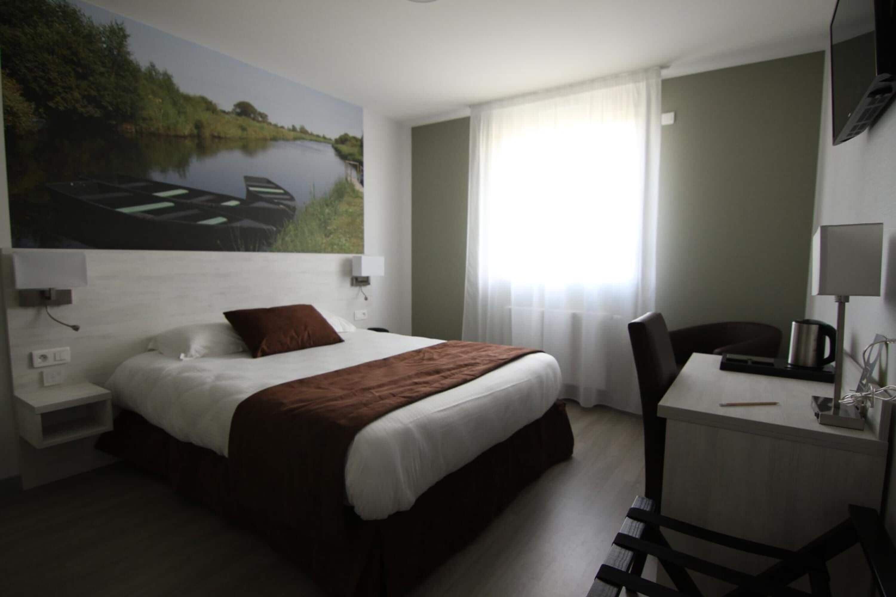 Una camera d'albergo con un letto, una scrivania, una sedia, una televisione e un quadro raffigurante un paesaggio fluviale.