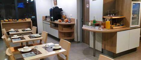 Un comedor moderno con mesas y sillas de madera, una estación de café y un refrigerador con puerta de vidrio.