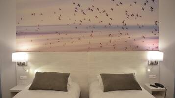 A hotel room with two beds, each with a pillow and a bedside table with a lamp and a phone.