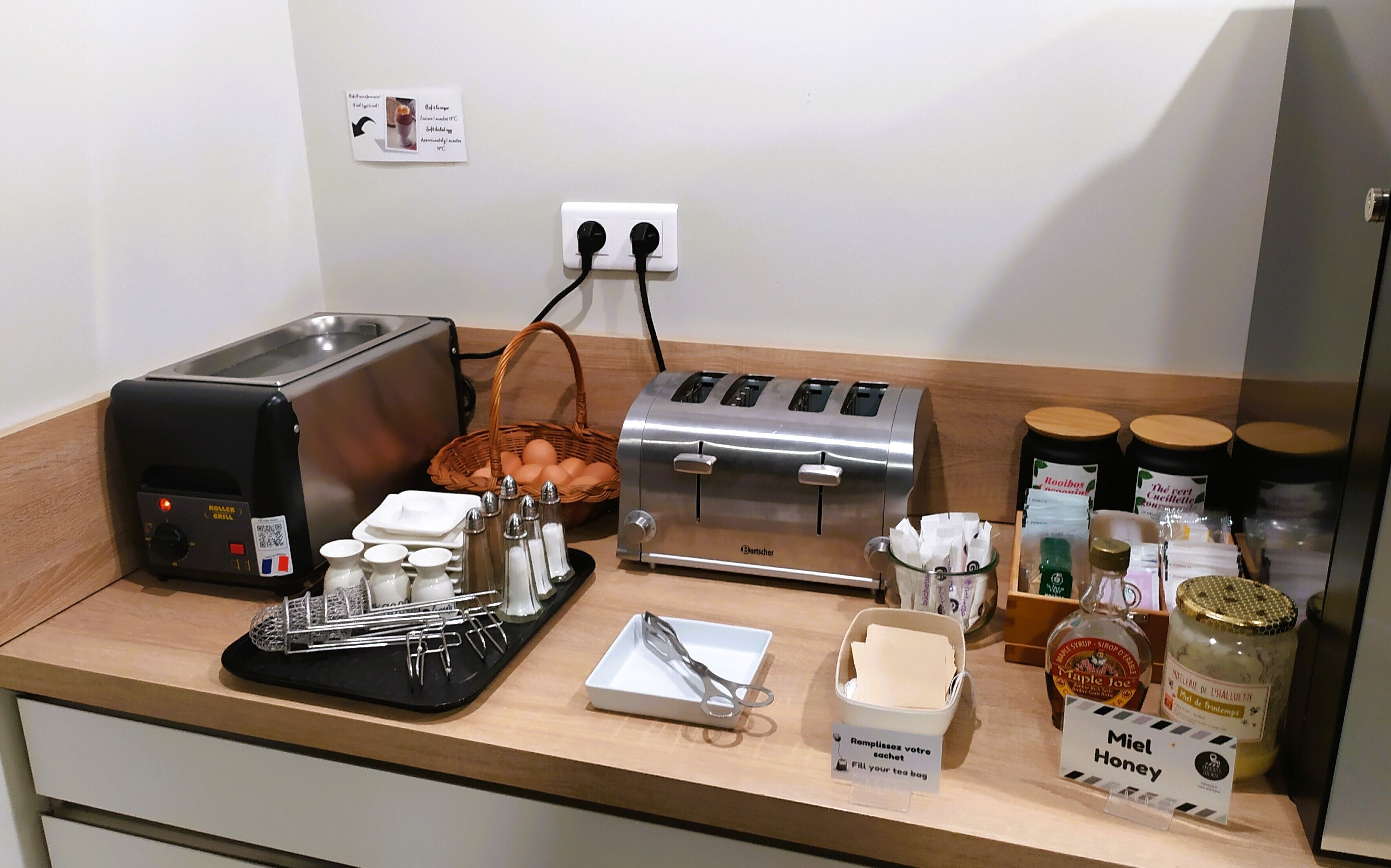 A kitchen counter with a toaster, a kettle, a basket of eggs, salt and pepper shakers, a tea bag dispenser, and jars of honey and maple syrup.