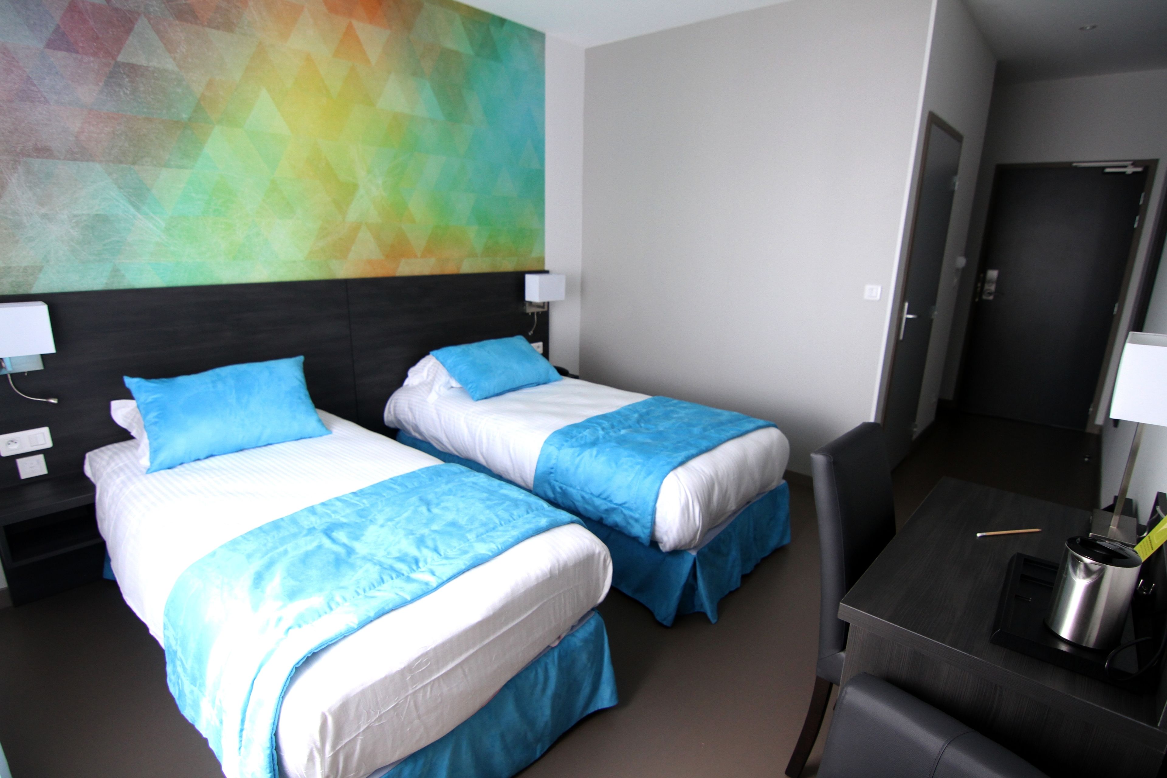 Ett hotellrum med två sängar, ett skrivbord och en färgstark, abstrakt målning på väggen.